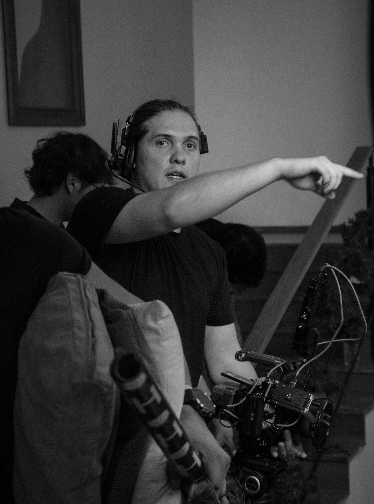 Black and white photo of a film crew member wearing headphones pointing direction on a movie set.