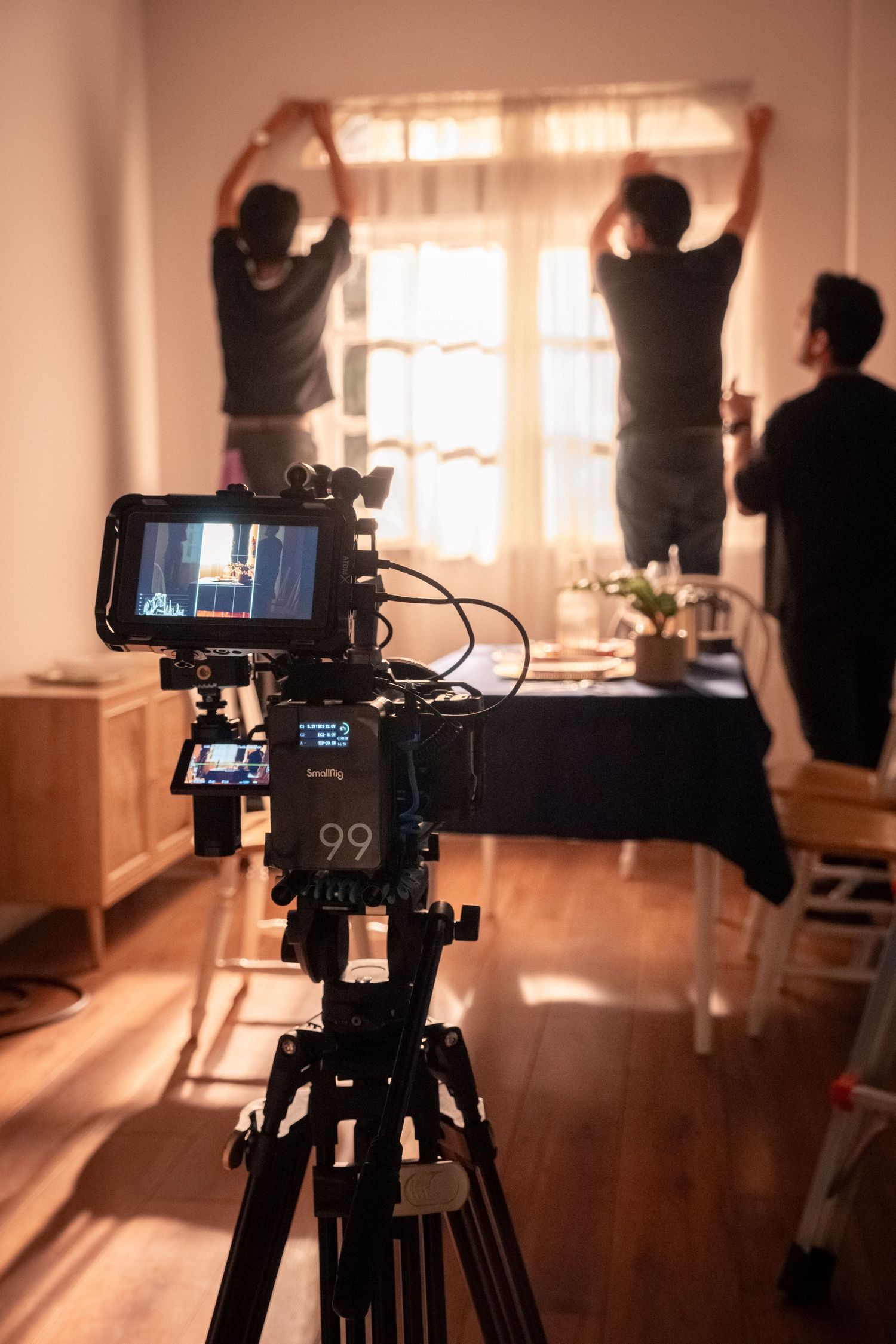 Camera monitor displays scene as crew members adjust curtains on a film production set.