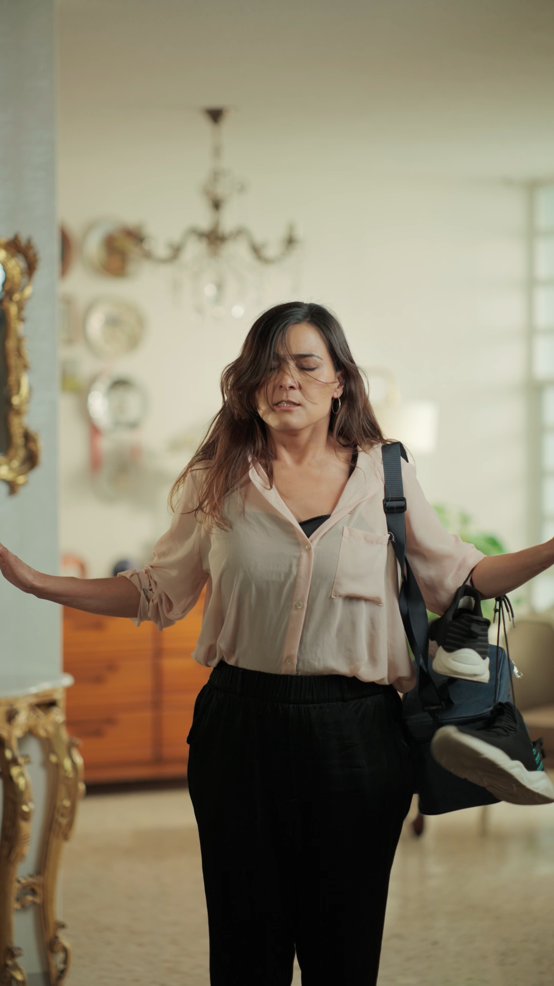 Woman with gym bag spreading arms in a vintage-style decorated living room.