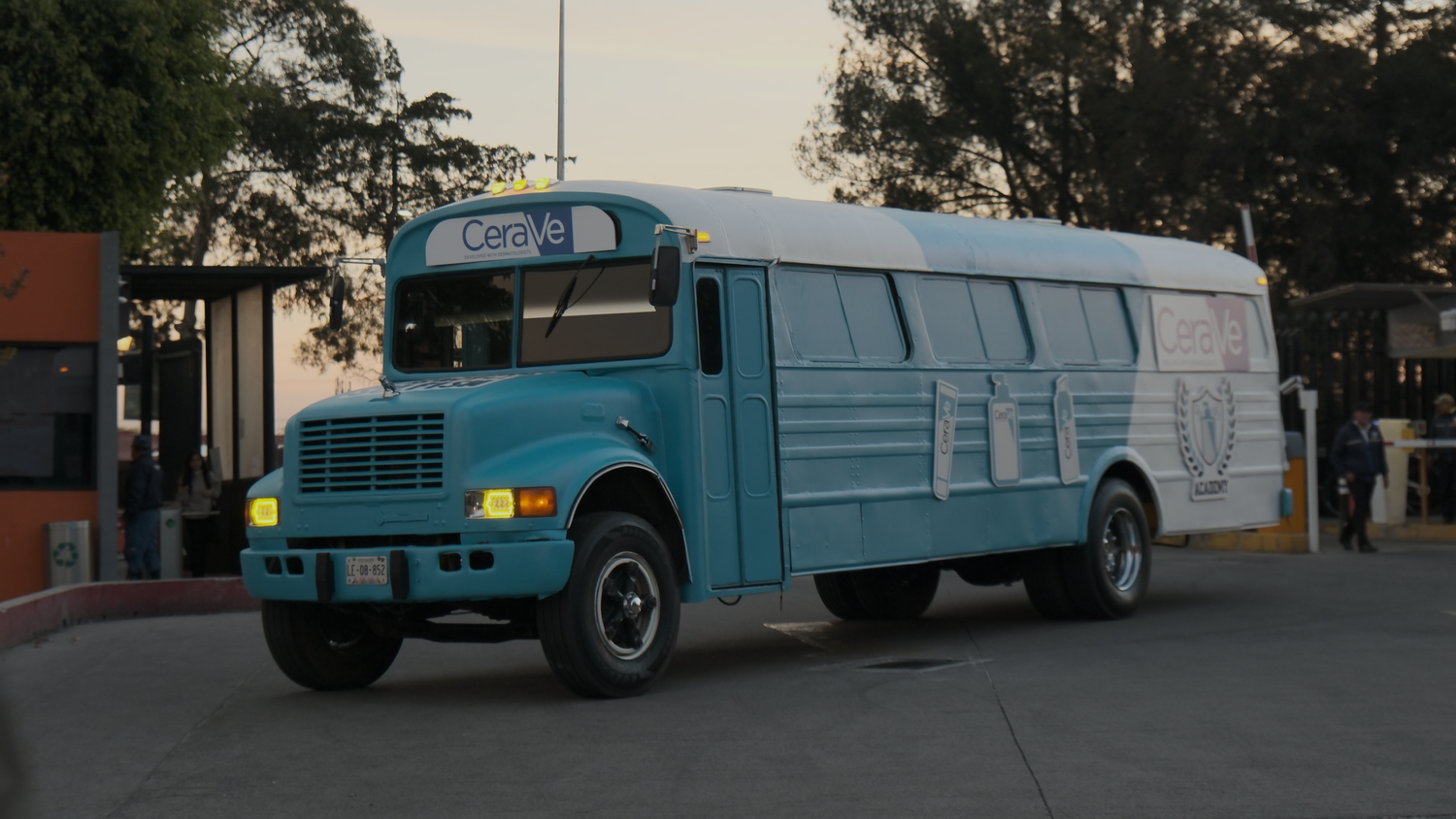 Turquoise vintage school bus with yellow headlights parked at gated entrance.