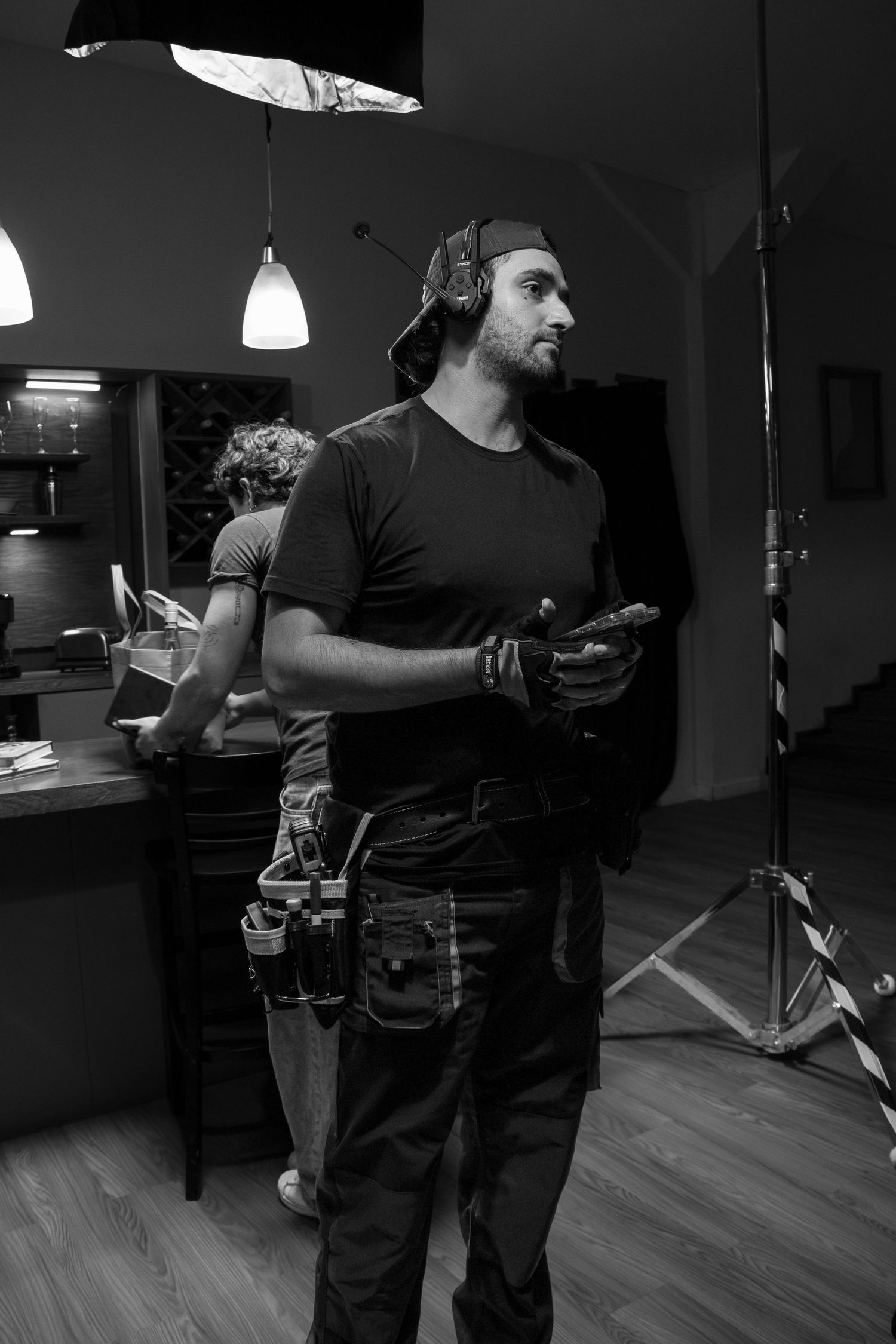 Male film crew member wearing headphones and tool belt stands on a professional movie set.