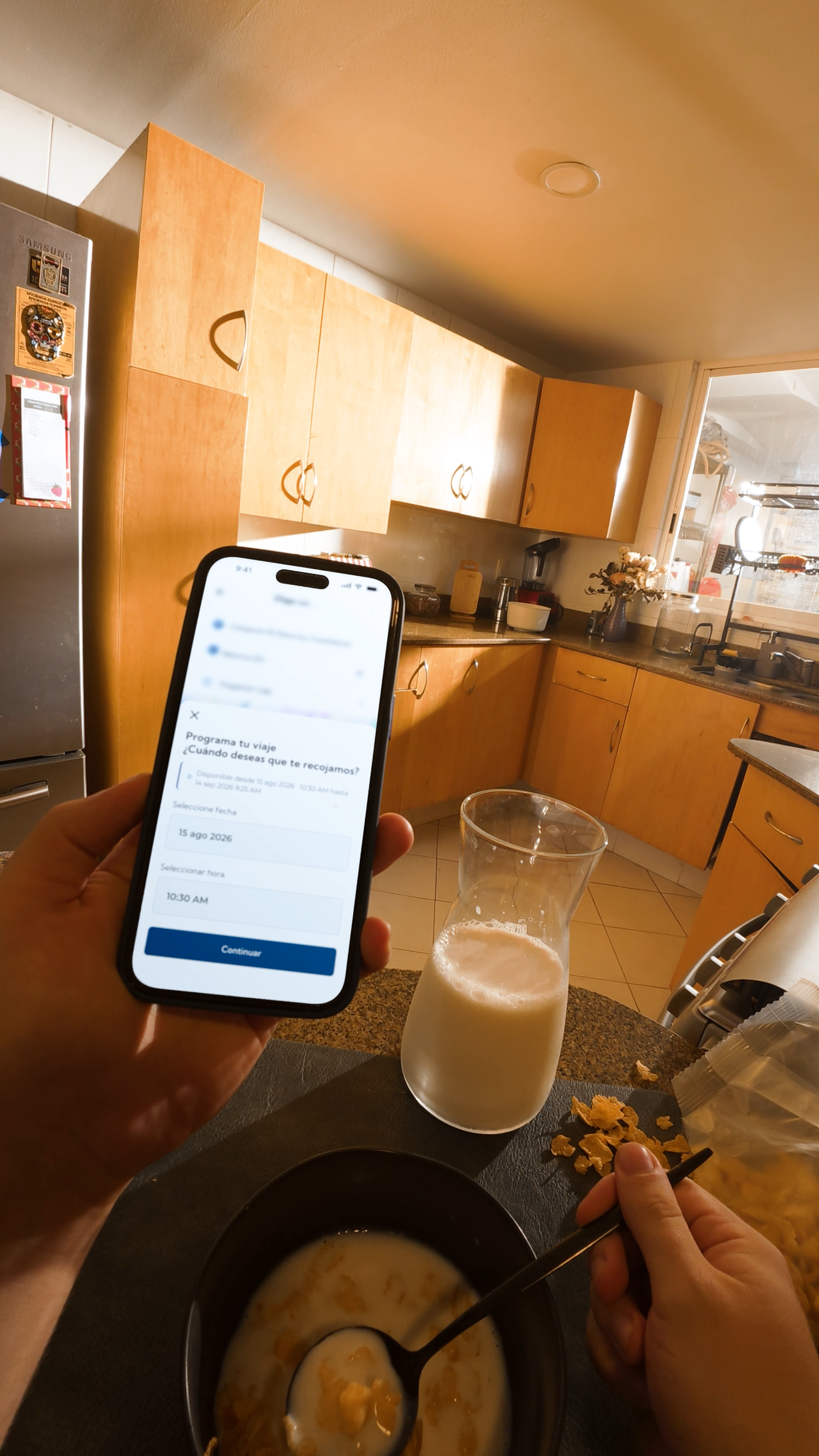 Person holding smartphone with app open while eating breakfast with milk in a kitchen.