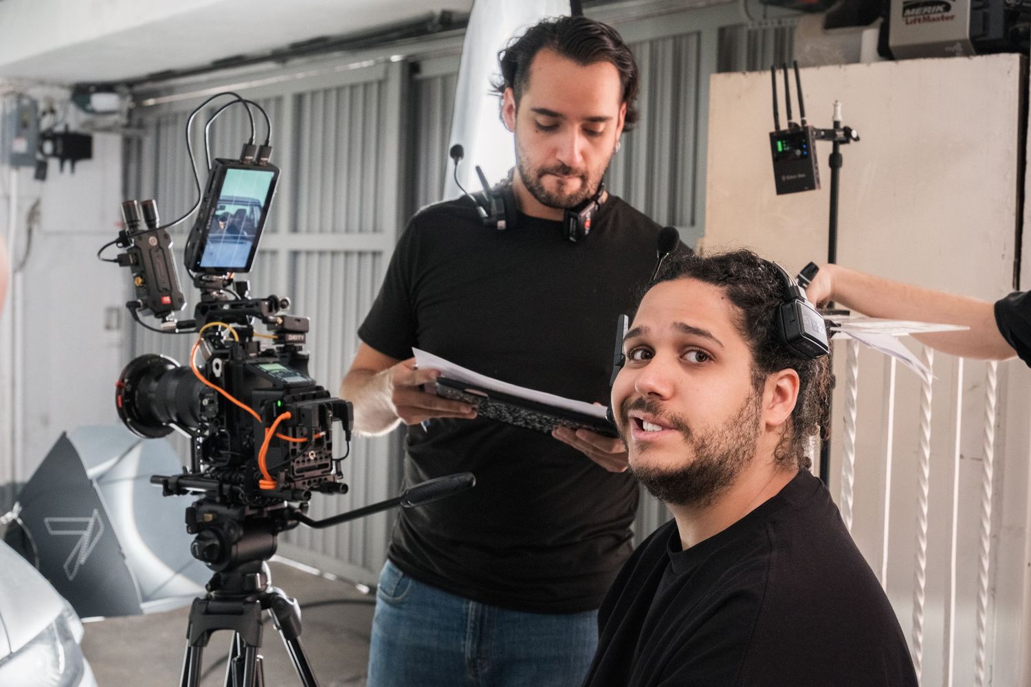Two male film crew members review a script next to a professional camera on set.