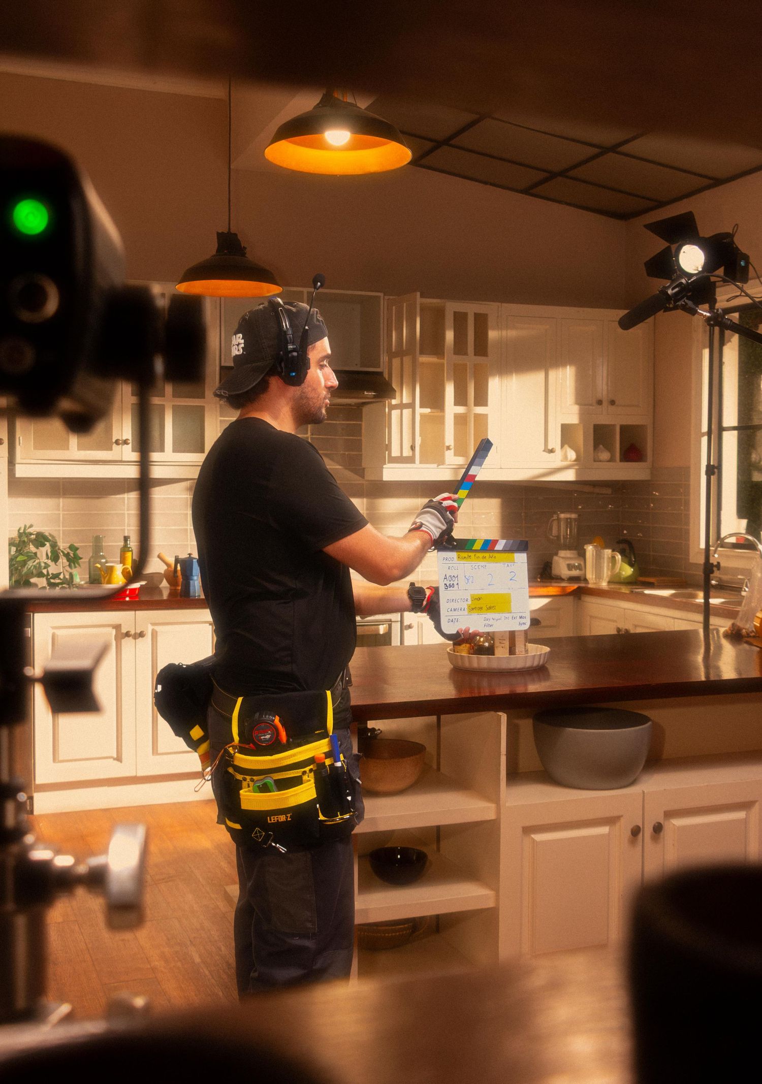 Film crew member holding a clapperboard prepares to slate a scene in a kitchen set.