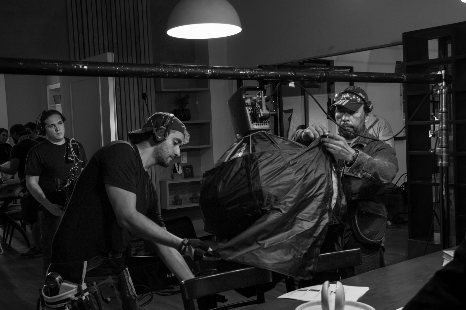 Black and white photo of film crew moving camera equipment on a professional indoor movie set.
