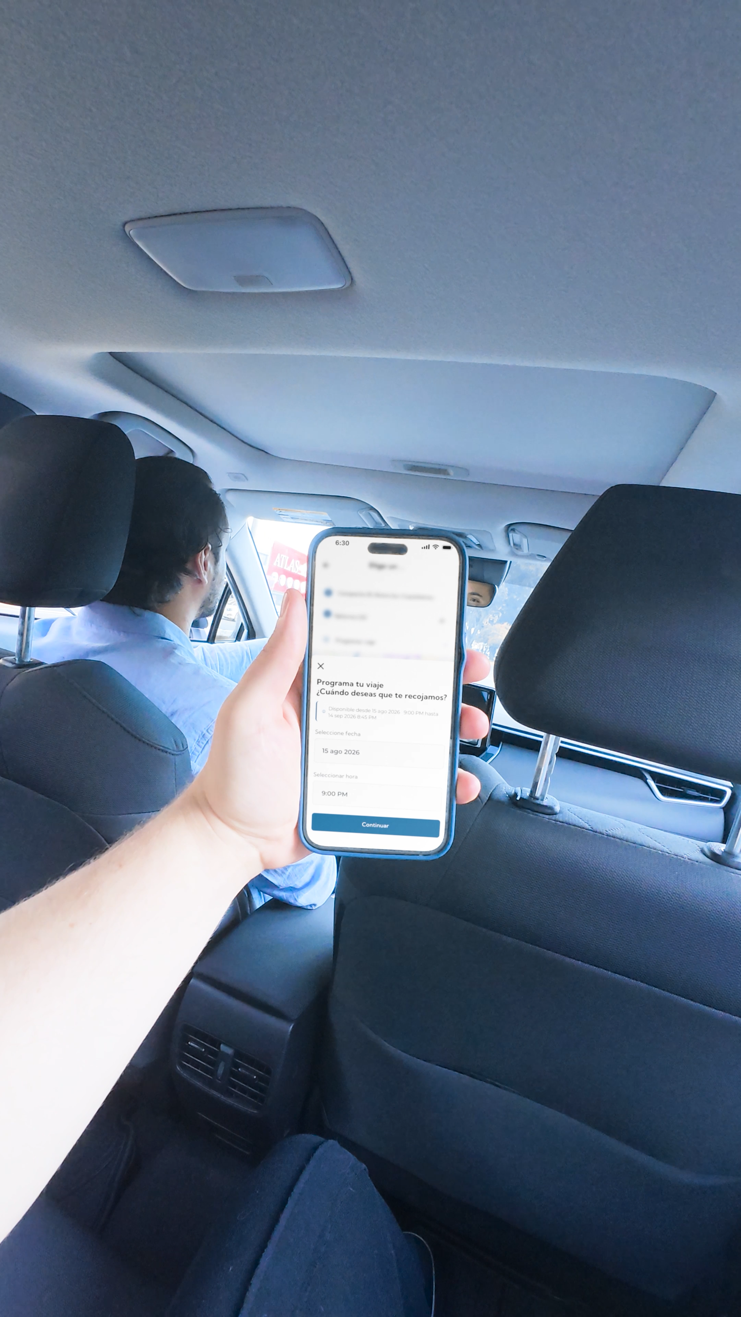 Passenger in backseat of car holding smartphone showing a mobile app screen.