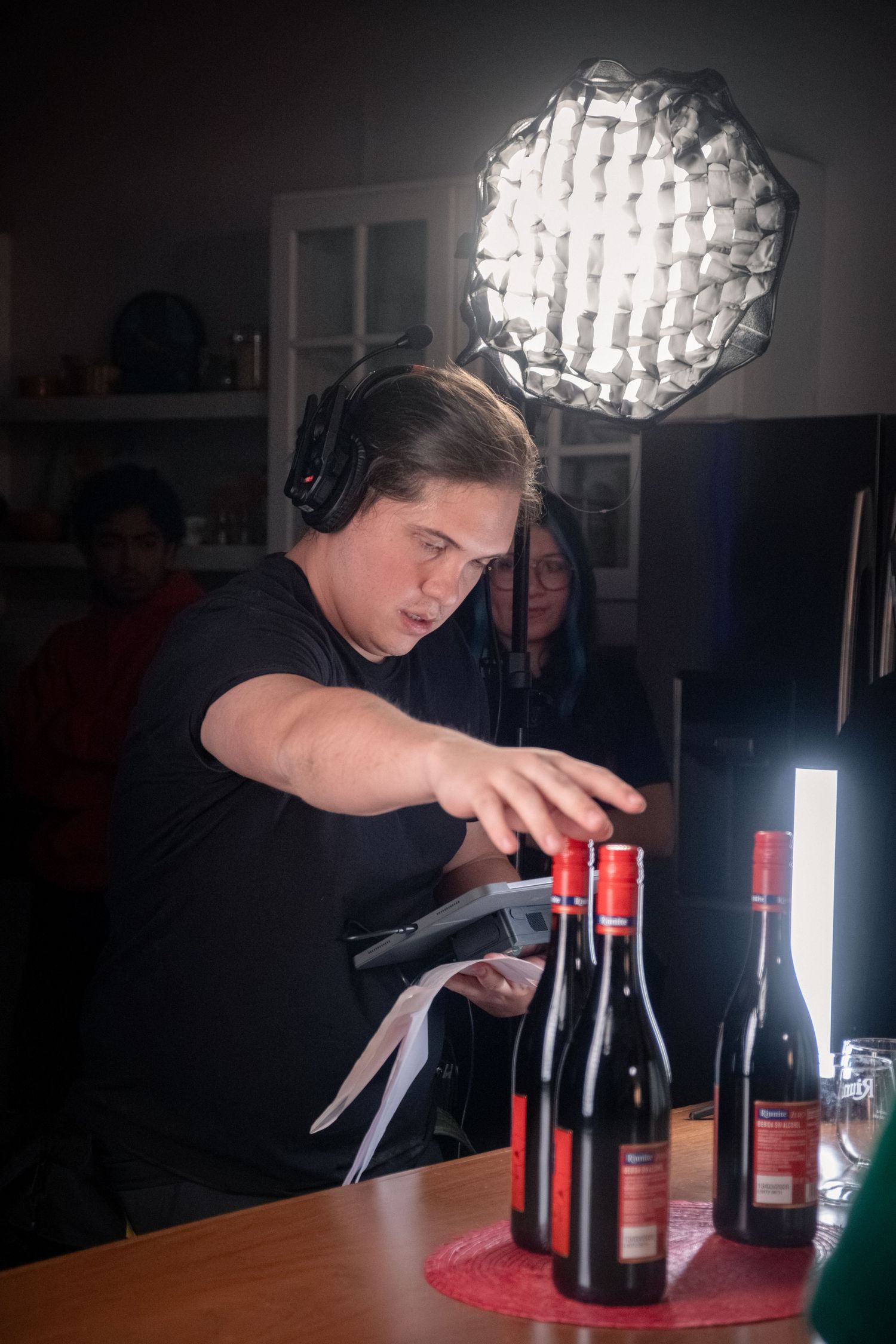 Camera operator adjusting wine bottles on a table under a softbox light during a film production.