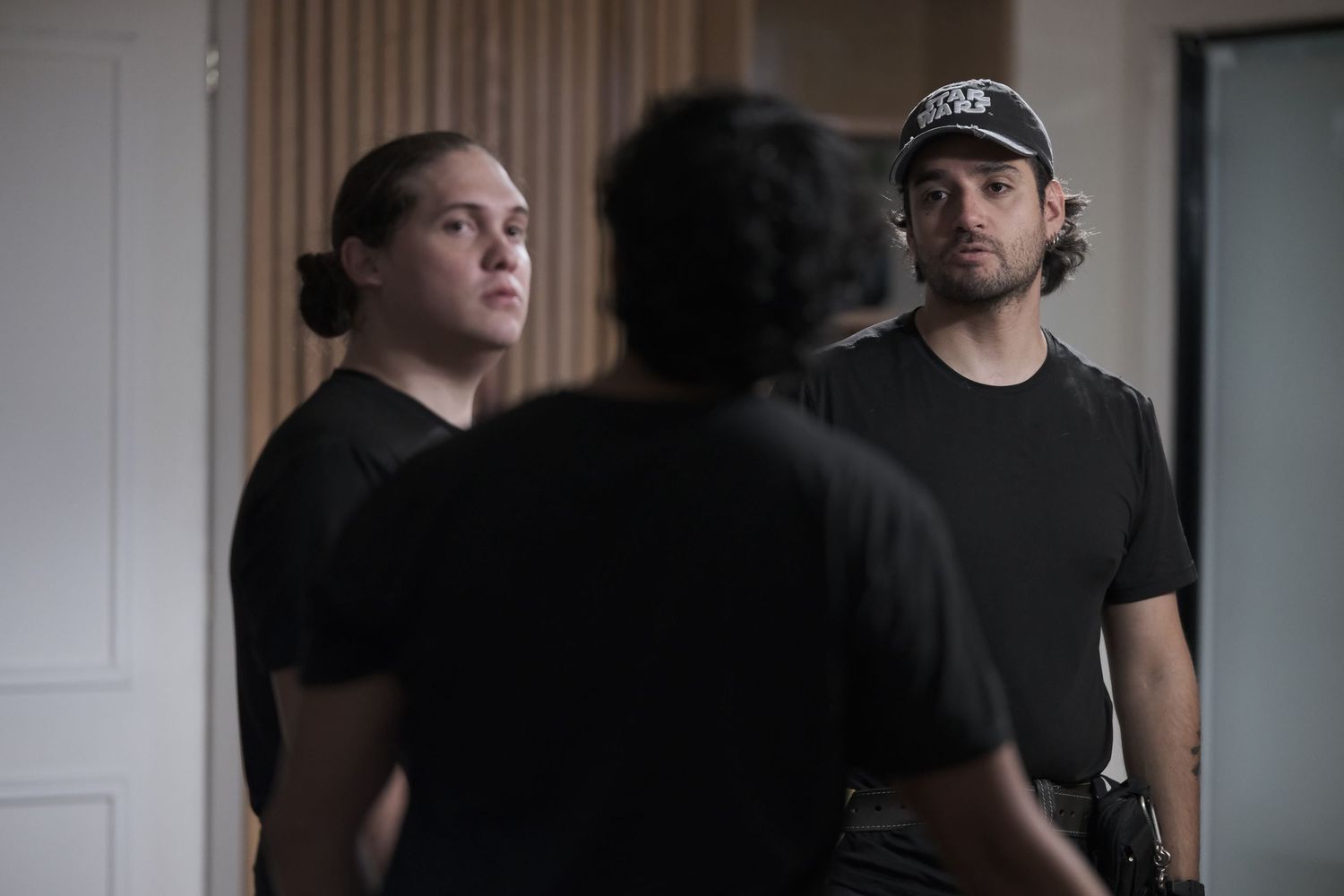 Three people in black shirts having a conversation in a modern indoor setting.
