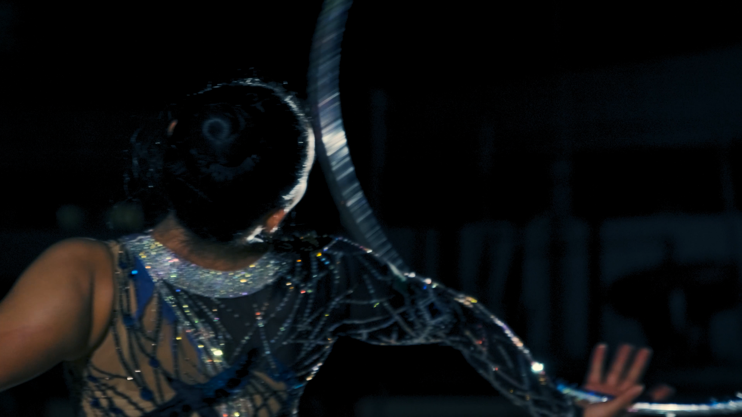 Close-up of rhythmic gymnast in sparkling leotard holding hoop in dark arena.