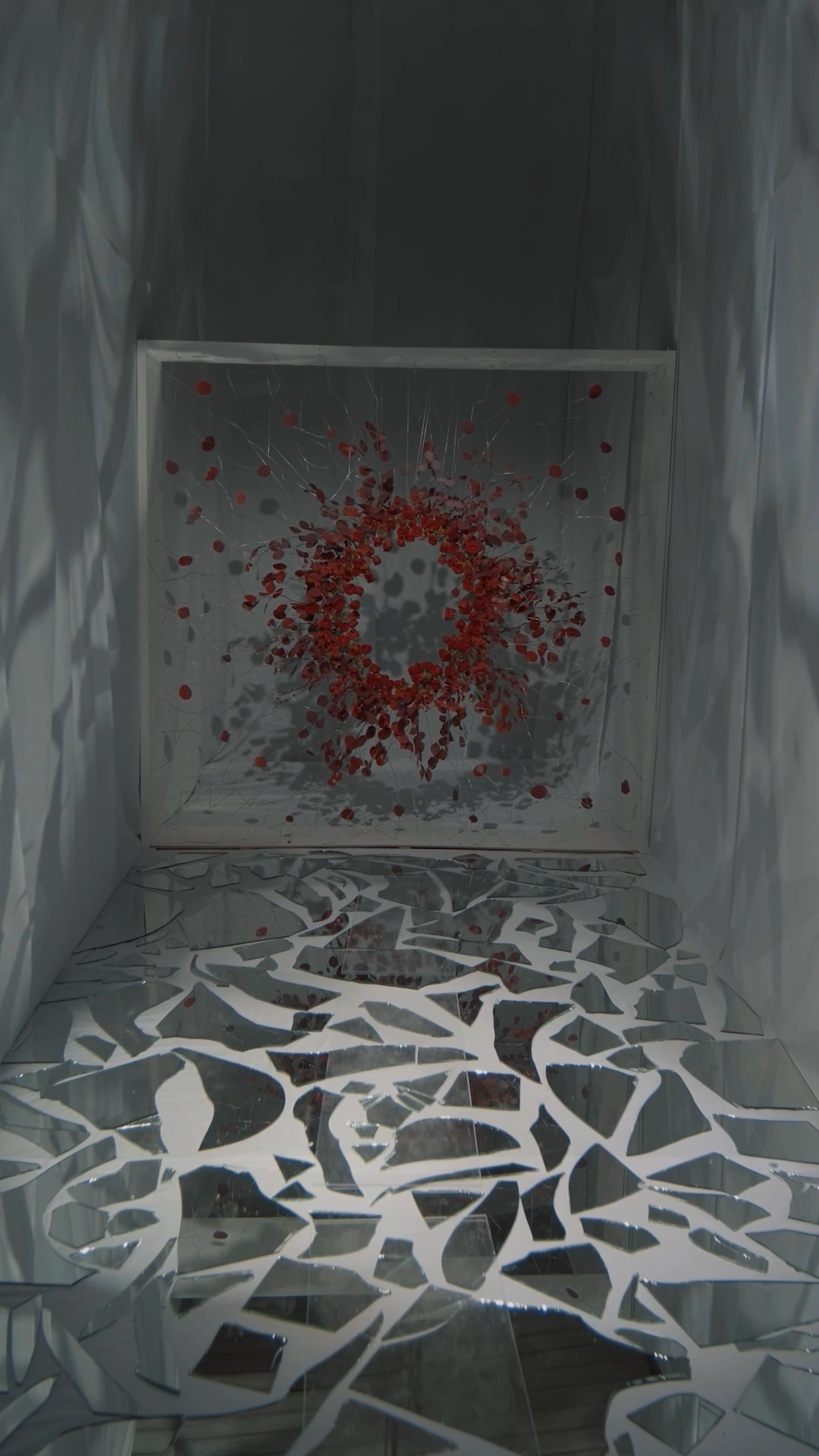 Abstract art installation featuring a red circular splatter on white wall with shattered mirror floor.