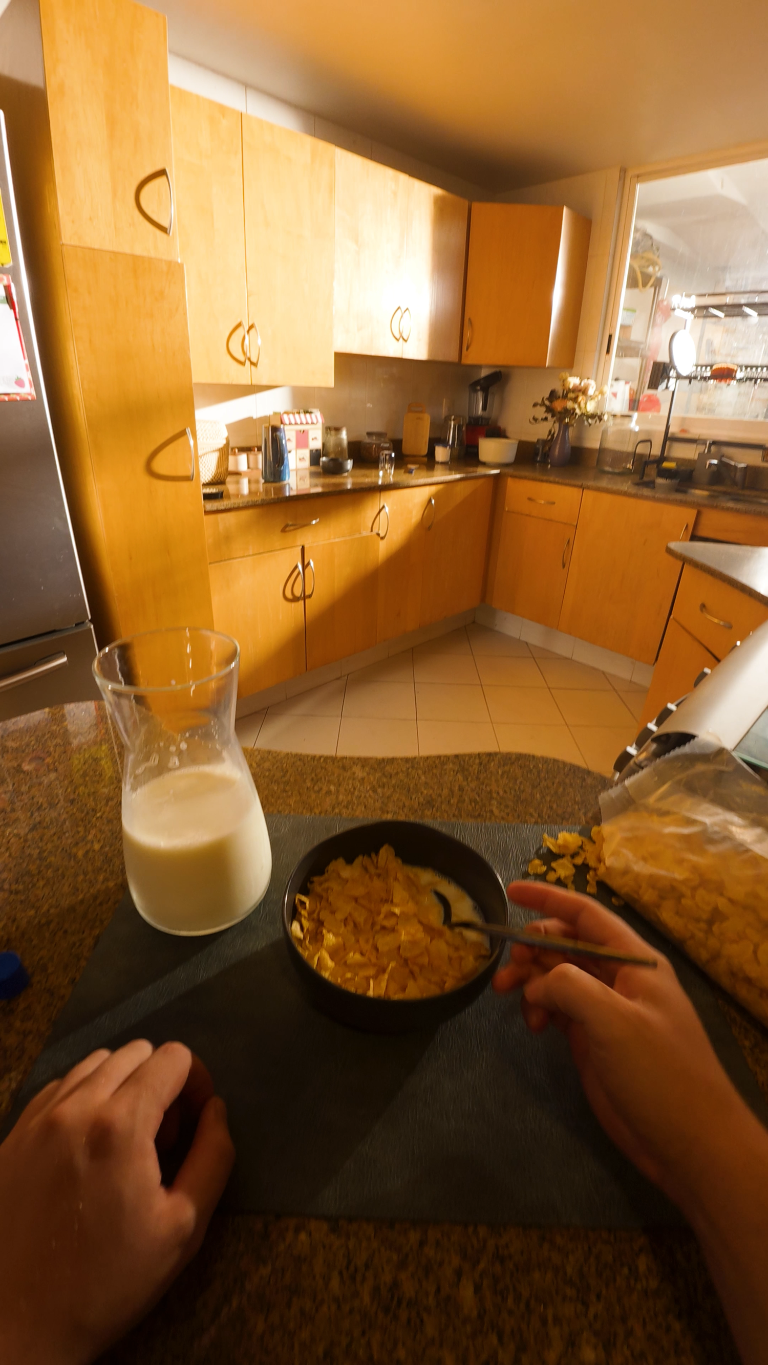 First-person view of person pouring cereal into bowl with milk jug in modern kitchen.