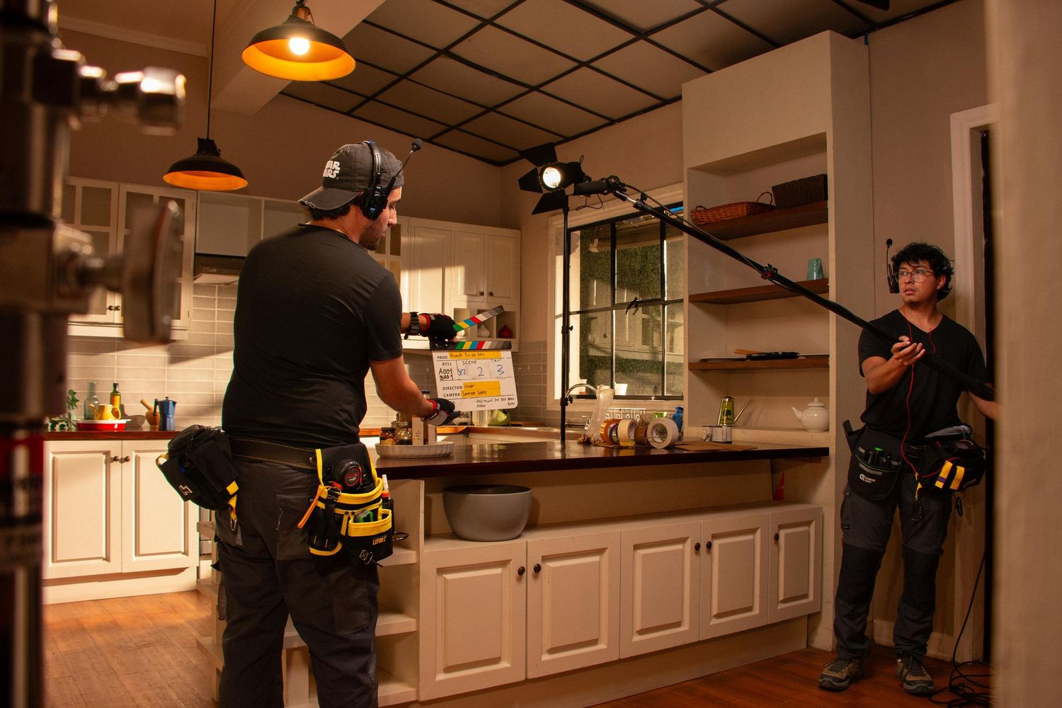 Film crew setting up lighting and boom microphone in a kitchen scene during video production.