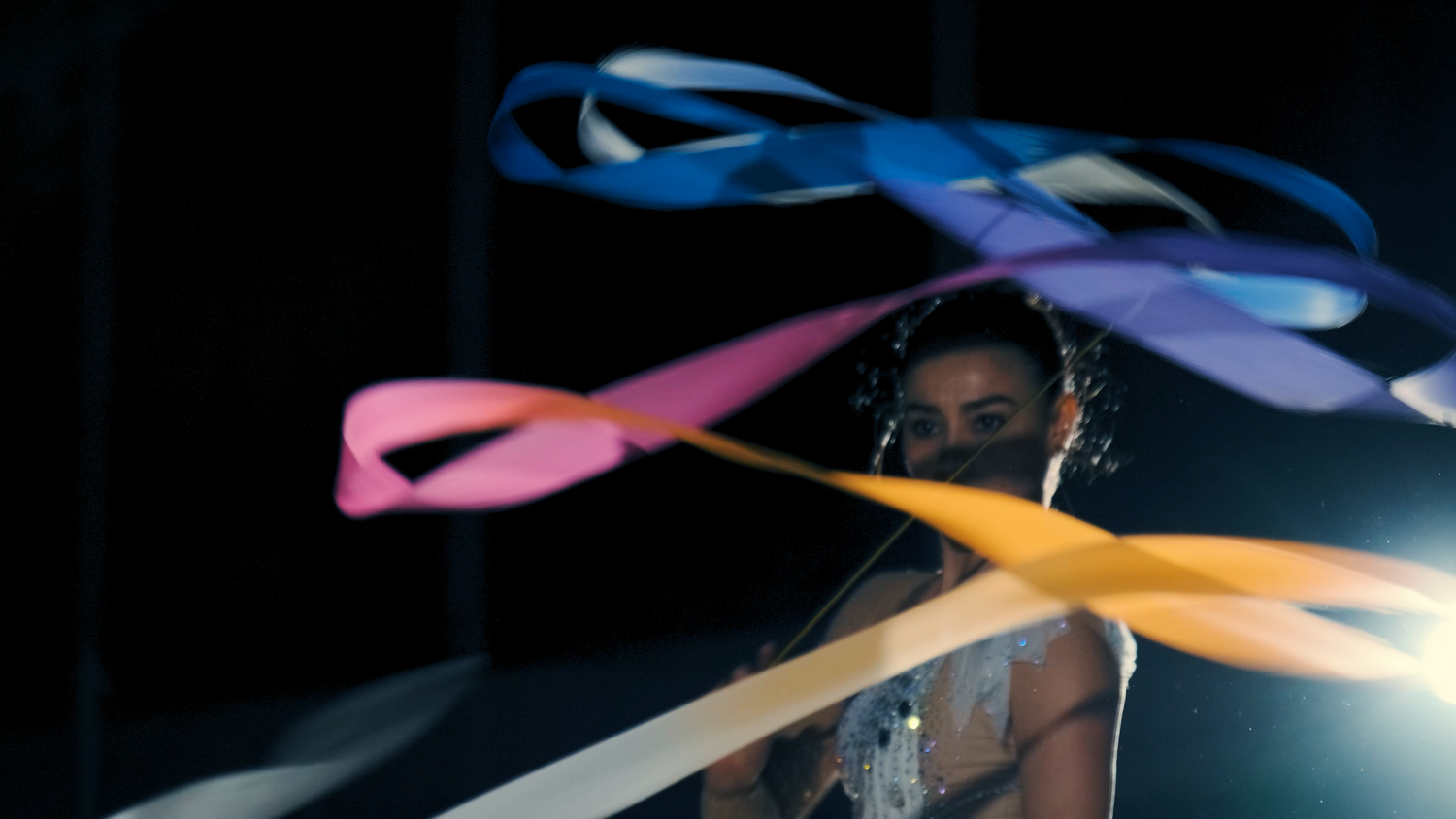 Colorful ribbons in blue, pink, and yellow swirl through the air during rhythmic gymnastics routine.