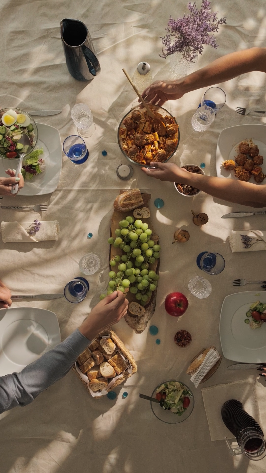 Aerial view of dining table with grapes, salads, bread and shared dishes during meal.