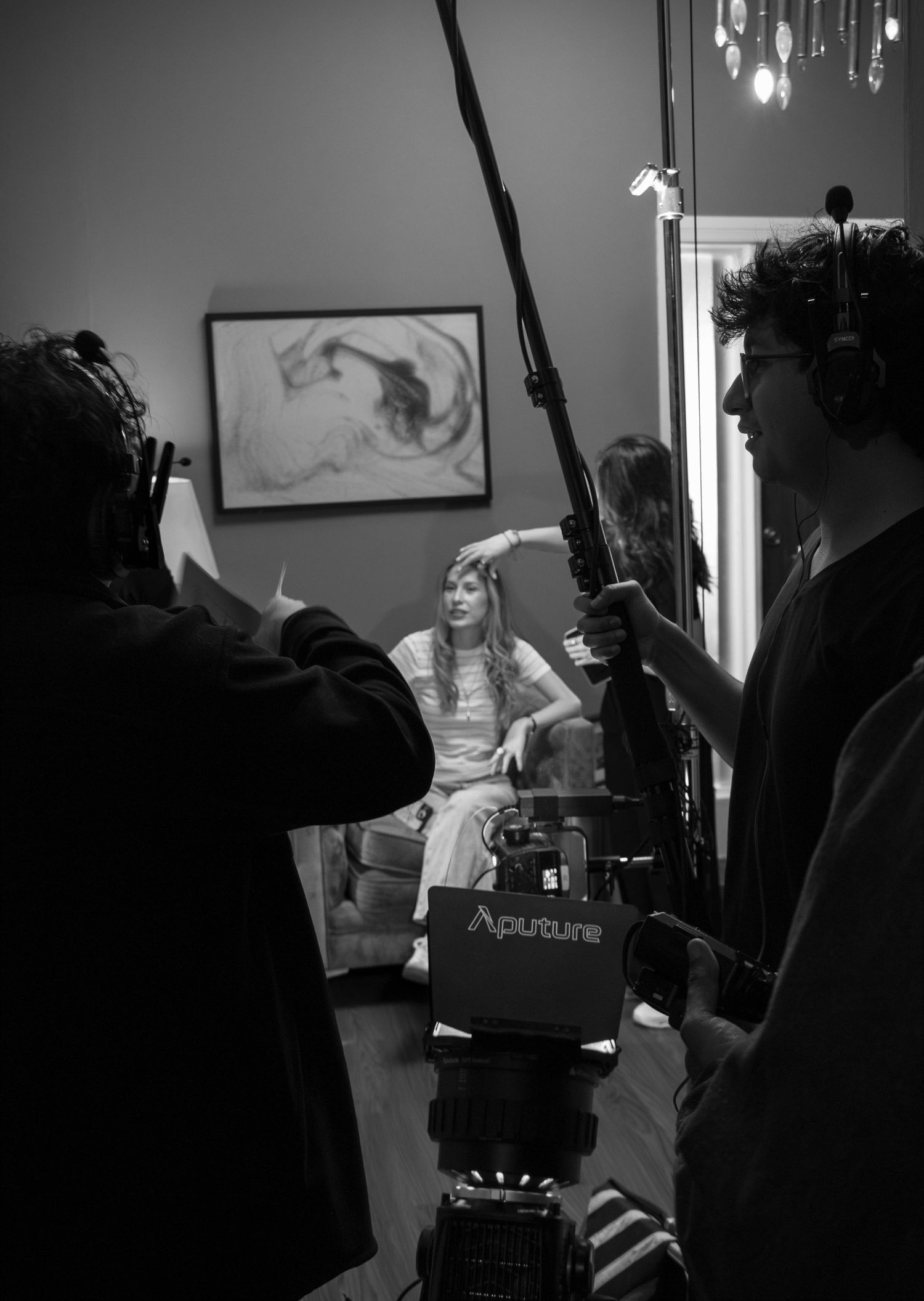 Black and white BTS shot of film crew with boom mic and Aputure light filming a seated actress.