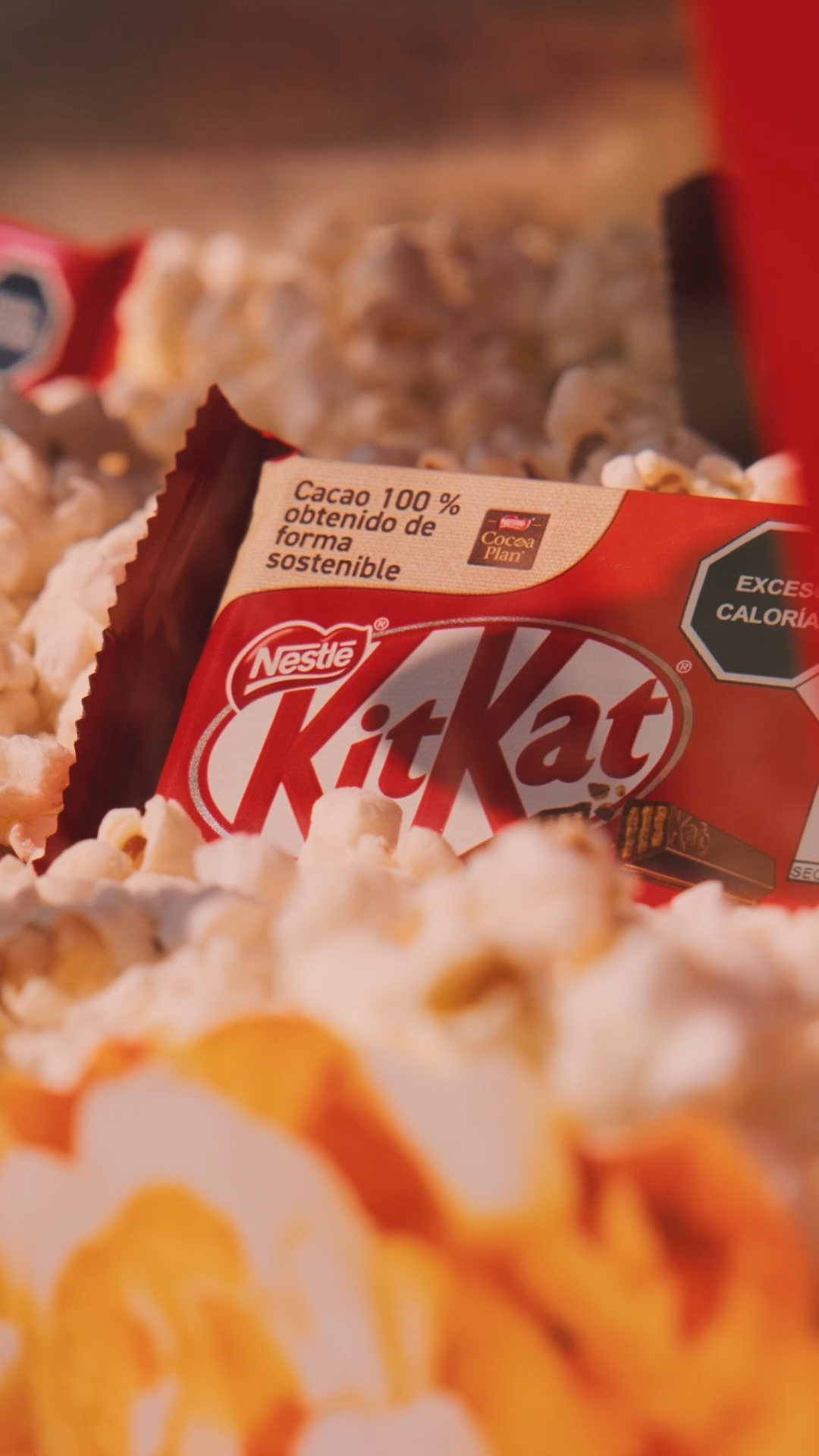 KitKat chocolate bar resting on fresh popcorn with Spanish text reading cacao 100% obtenido de forma sostenible.