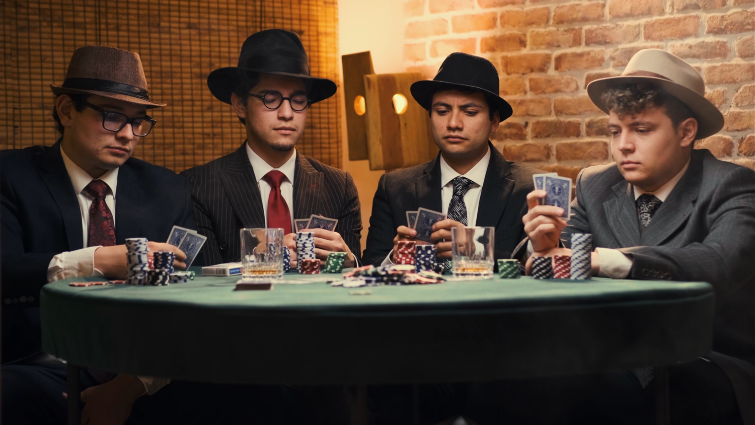 Four young men in suits and fedora hats playing poker at green felt table with chips.