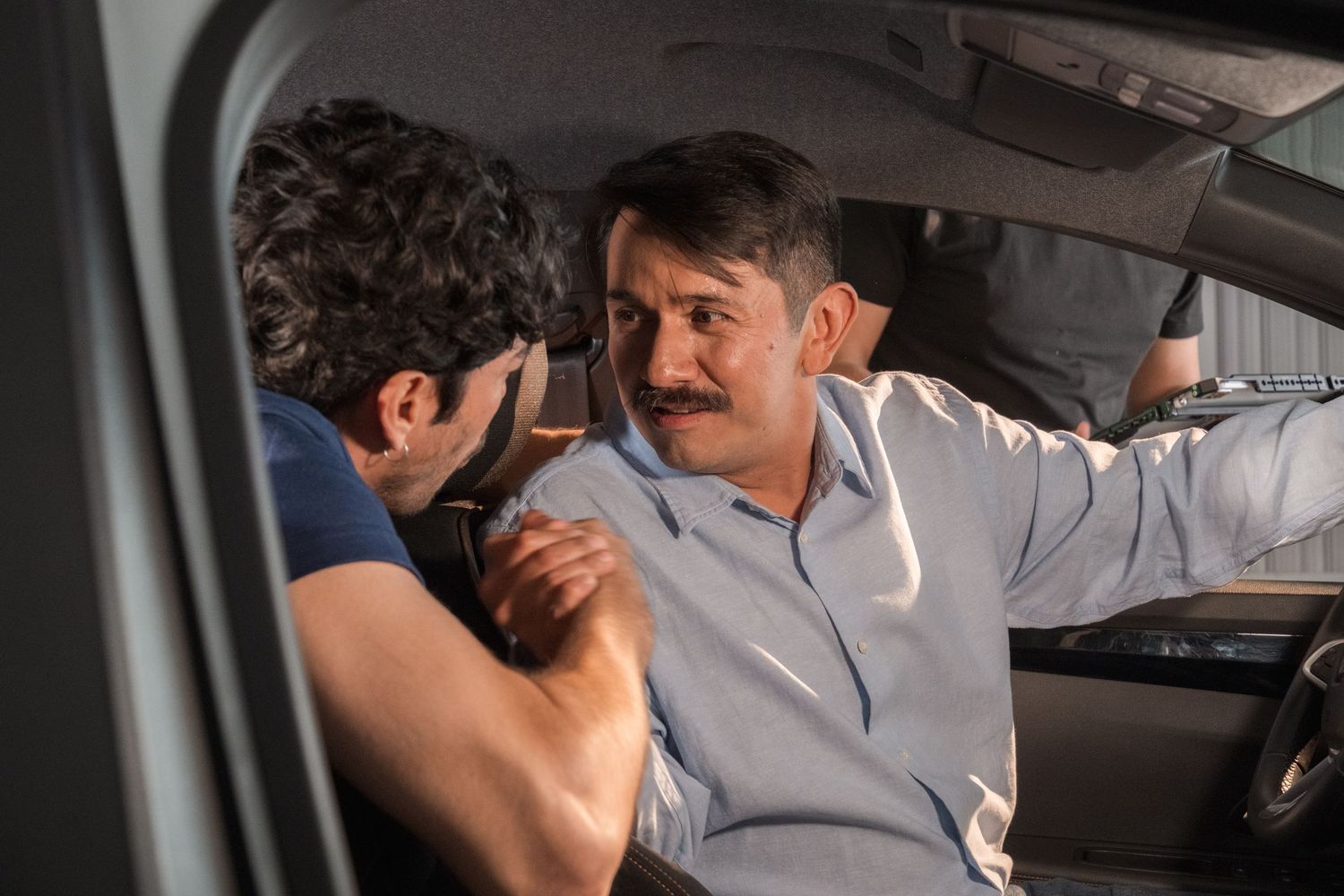 Two men having an intense conversation inside a car during a film scene.