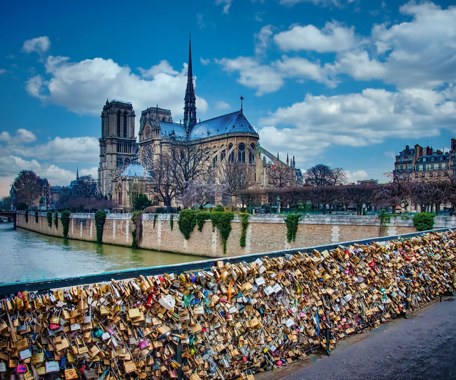 Notre Dame Cathedral in Paris viewed across the Seine River with colorful love locks on a bridge railing.