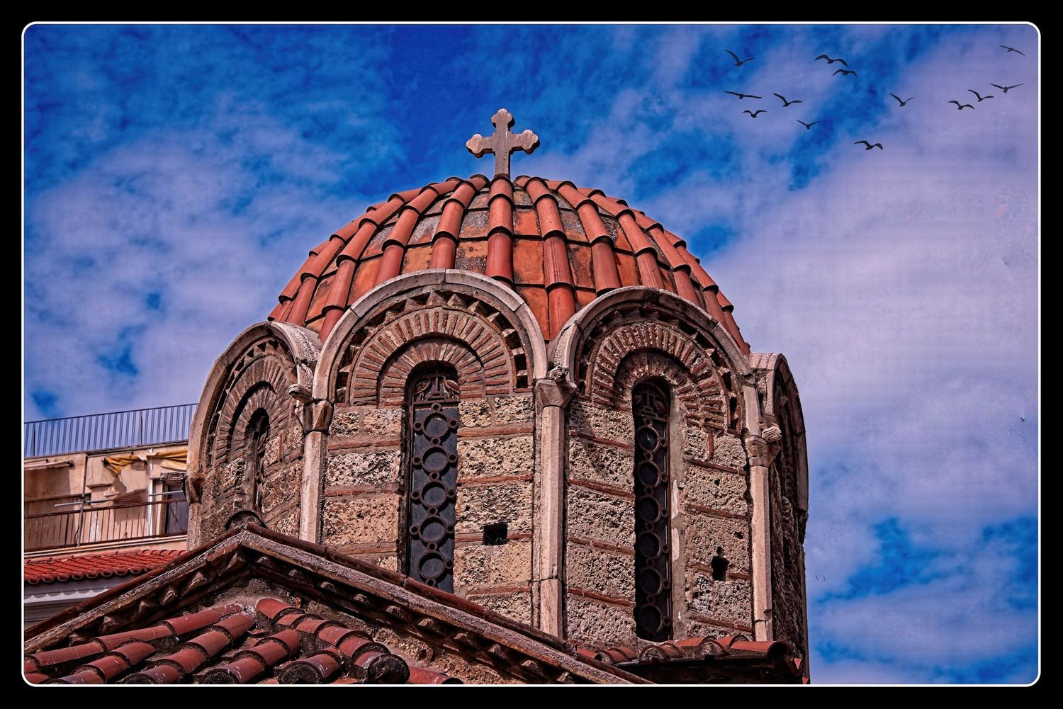Byzantine church dome with red terracotta tiles and cross against a blue cloudy sky in Athens, Greece.