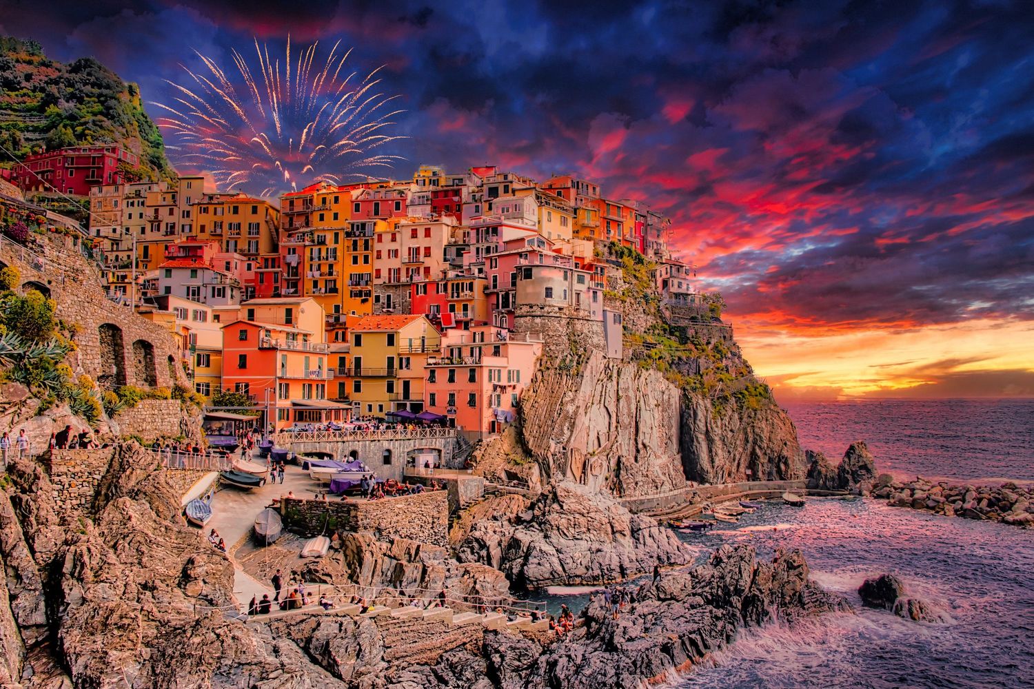 Manarola Cinque Terre village glows with colorful buildings on rocky cliffs at sunset with festive fireworks overhead.