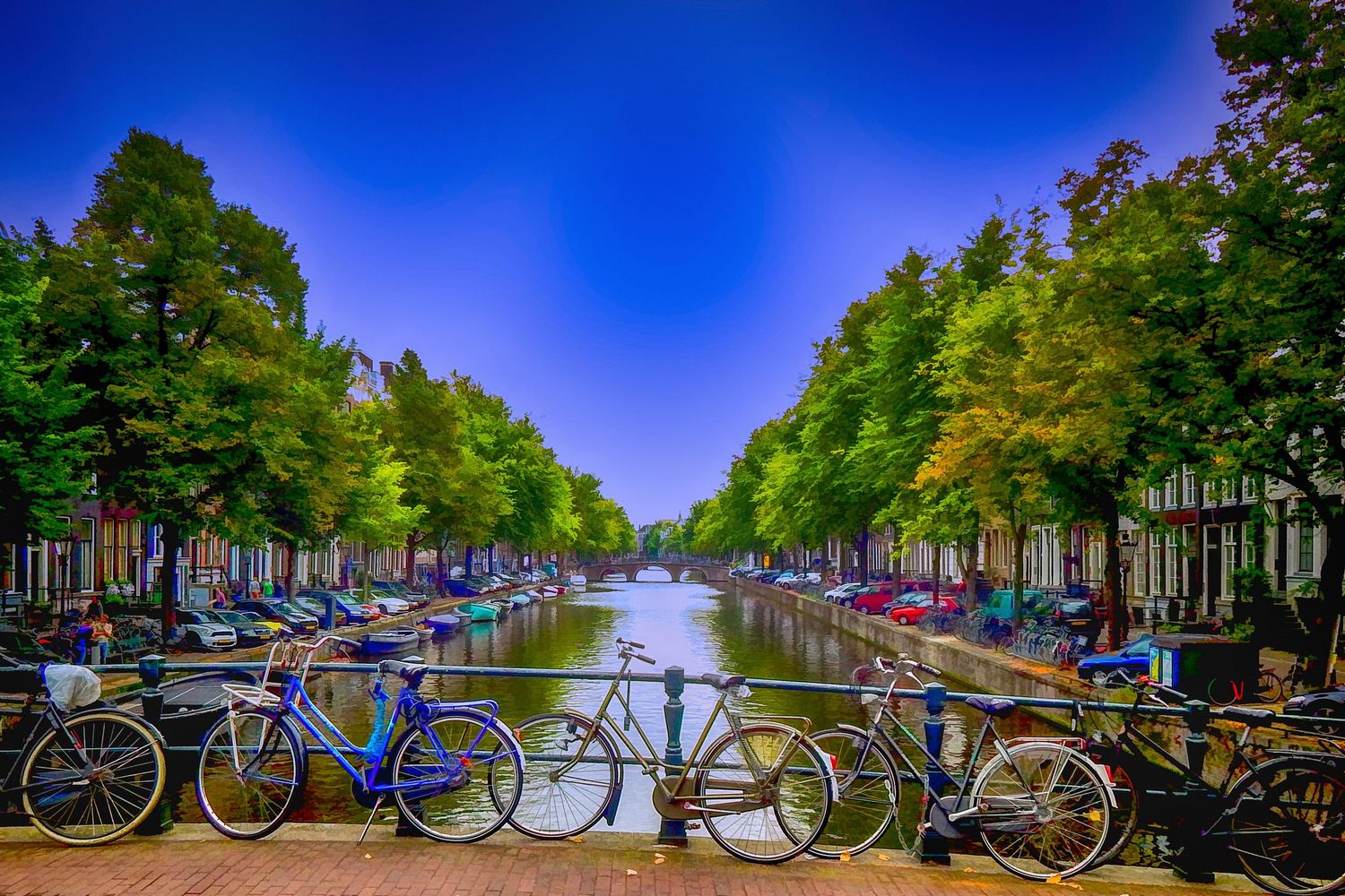 Bicycles parked on a bridge over a scenic Amsterdam, The Netherlands, canal lined with trees and boats.