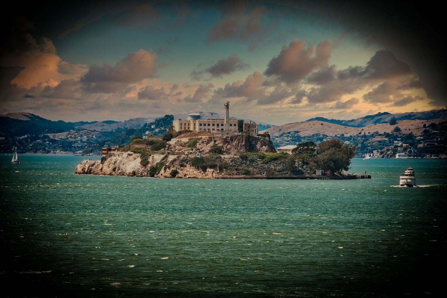 Alcatraz Island prison, through a telescope, surrounded by choppy green waters of San Francisco Bay under a dramatic cloudy sky.