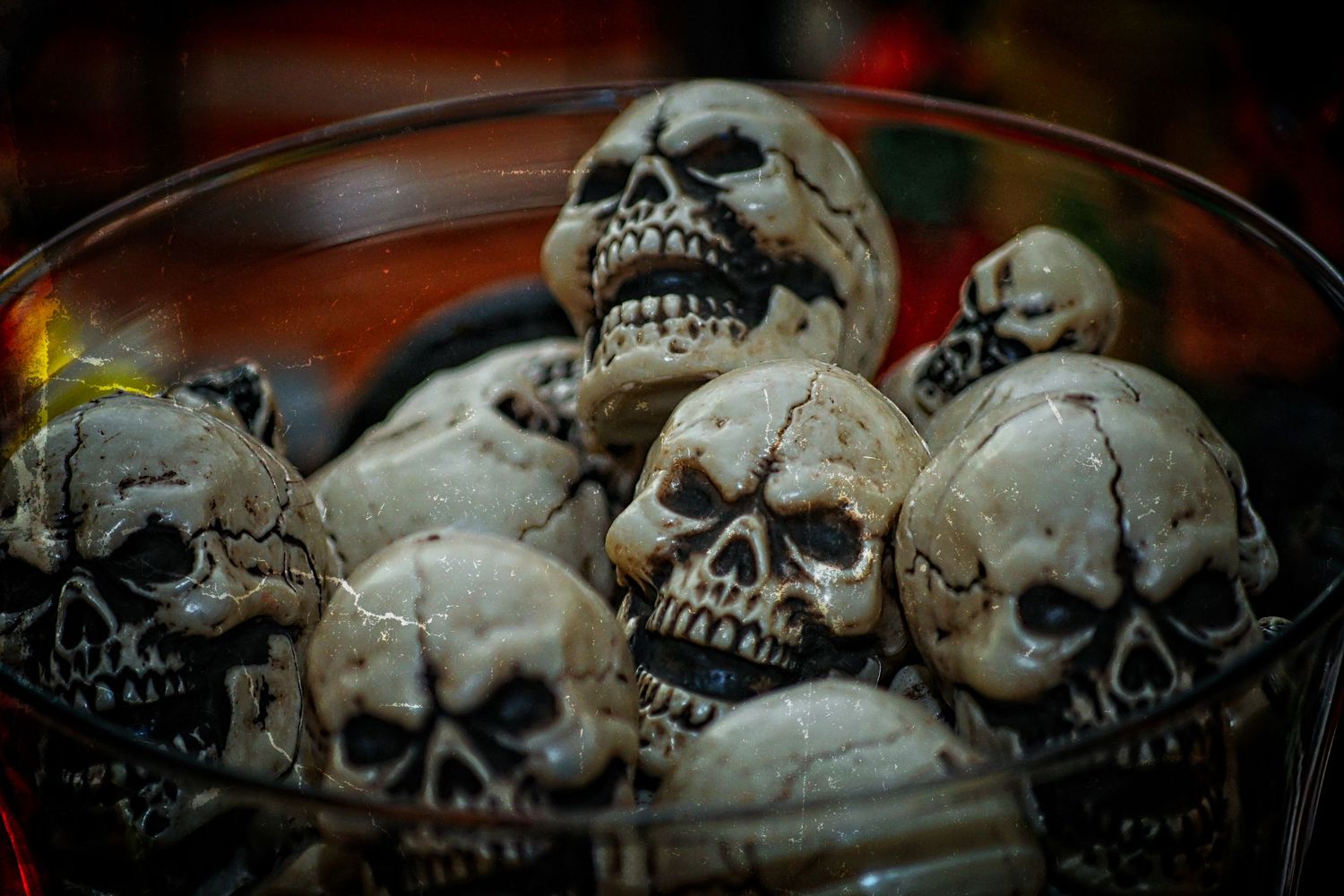 Collection of decorative Halloween skull replicas piled in a glass bowl display.