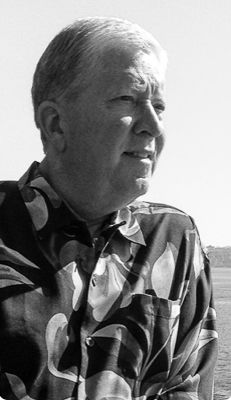 Black and white portrait of an older man with gray hair wearing a patterned shirt, gazing into the distance outdoors. Marty Faulkner.