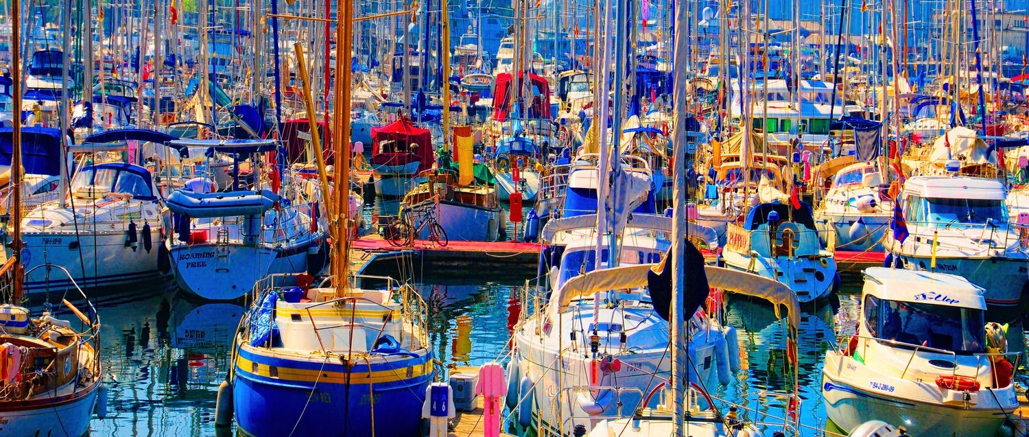 Colorful panoramic view of a crowded marina filled with vibrant blue and white sailboats and fishing vessels, Barcelona, Spain.