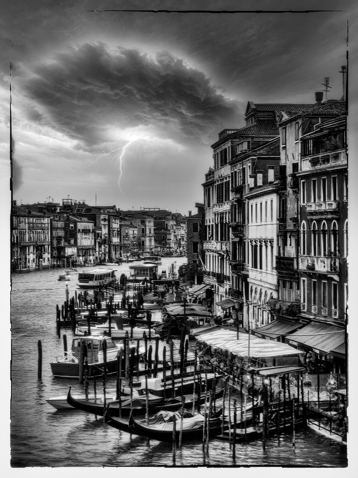 Dramatic black and white photo of Venice Grand Canal with gondolas and lightning storm over historic buildings.
