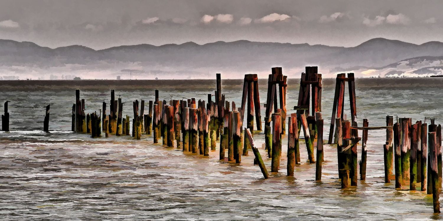Moody panoramic view of weathered wooden pier pilings standing in misty coastal waters with distant mountains, California.