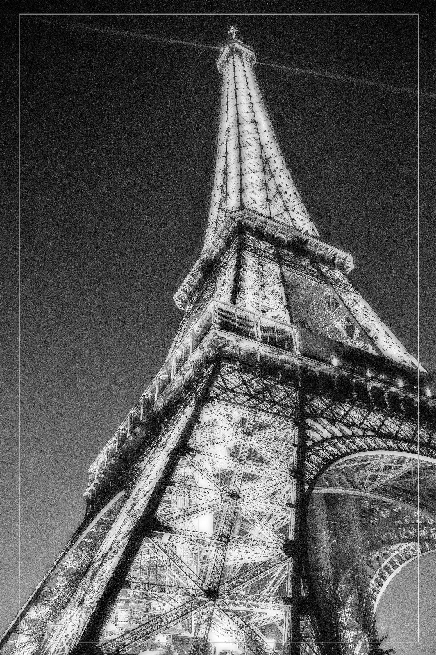 Low angle black and white night shot of the illuminated Eiffel Tower rising dramatically against a dark sky.