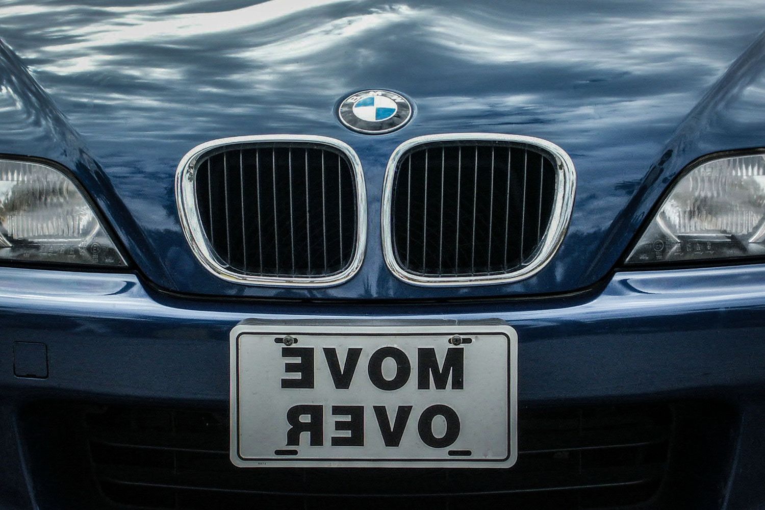 Front view of blue BMW car with reversed MOVE OVER license plate reflection.
