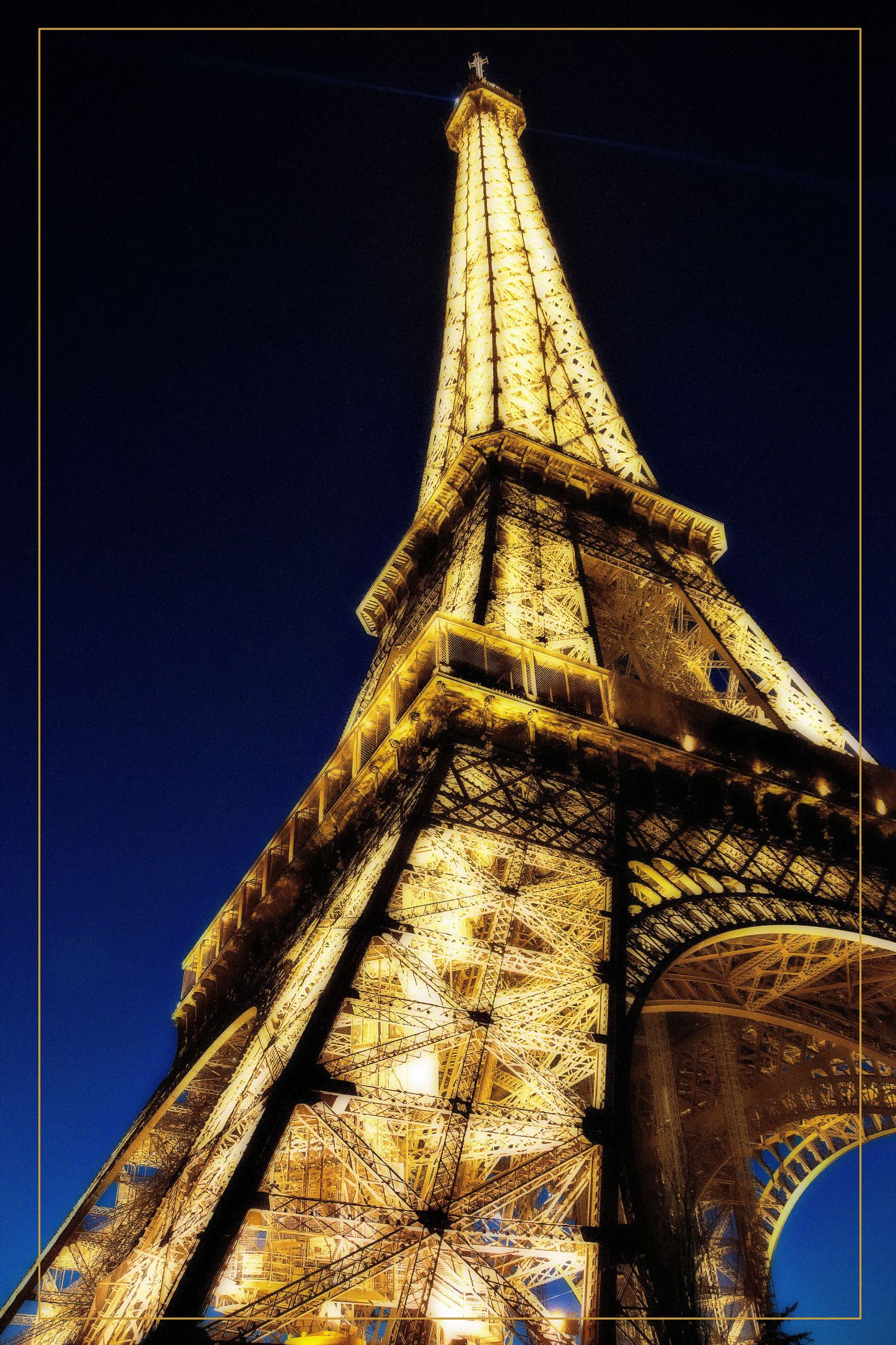 Eiffel Tower illuminated at night with golden lights against a deep blue sky, viewed from below in Paris, France.