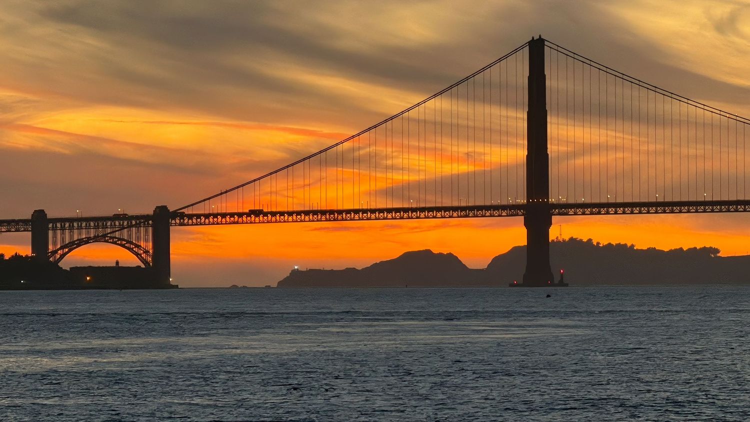Golden Gate Bridge dramatic silhouette against a fiery orange sunset sky over the bay. San Francisco, California.