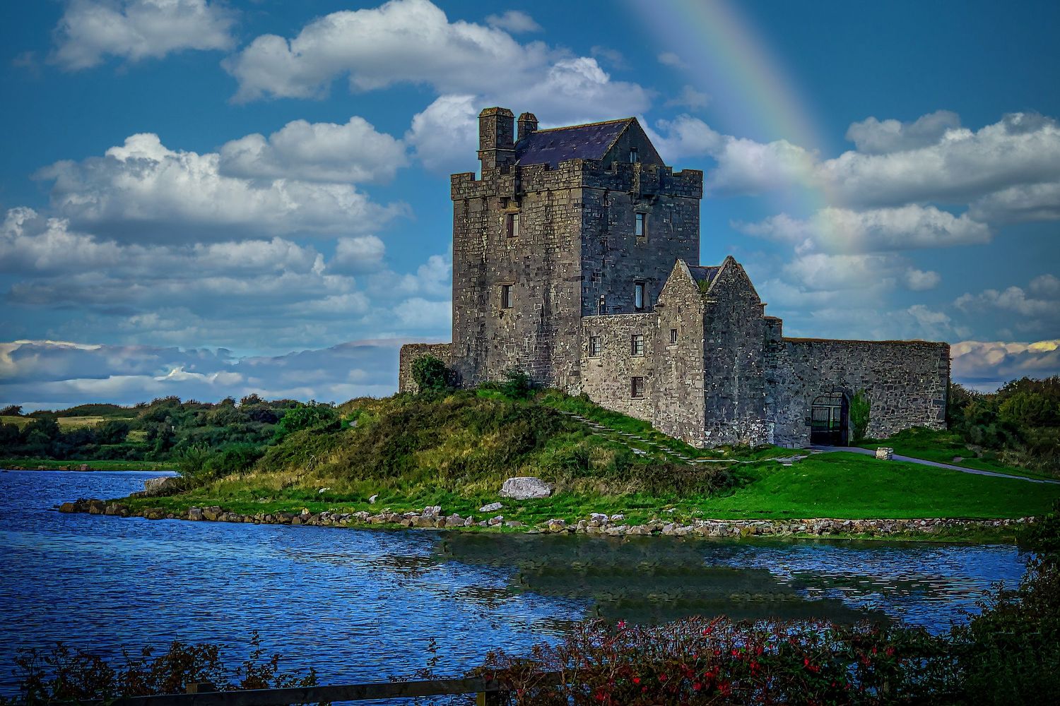 Medieval Dunguaire Castle reflected in calm waters under a dramatic cloudy sky in Ireland.