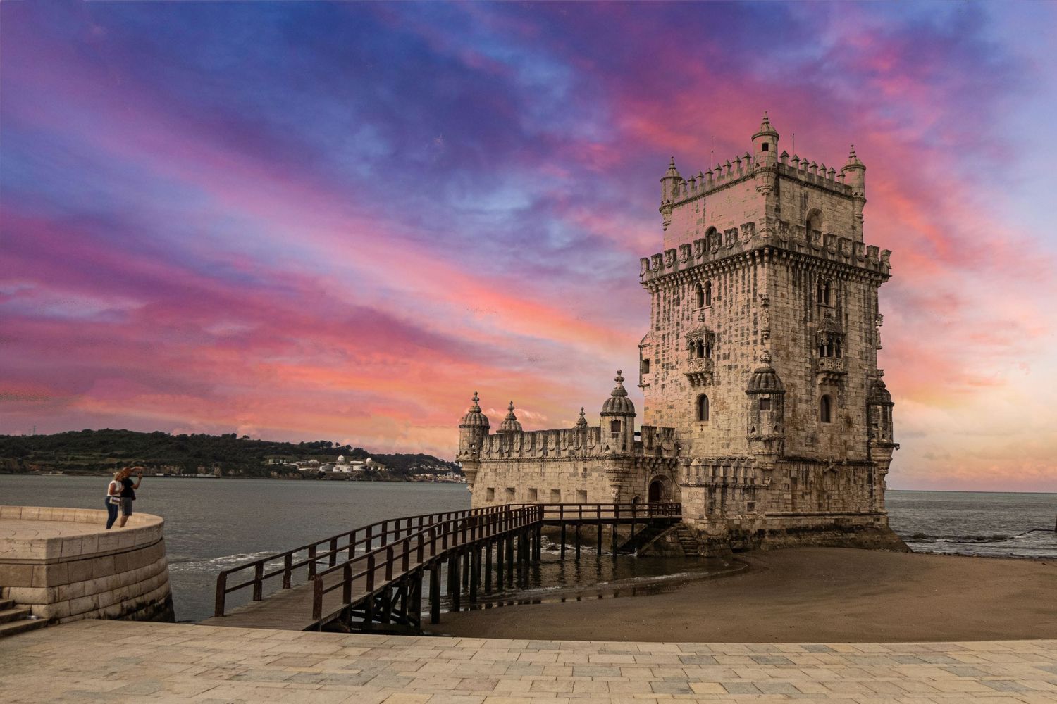 Historic Torre de Belem medieval tower in Lisbon Portugal at dramatic pink and purple sunset over the Tagus River.