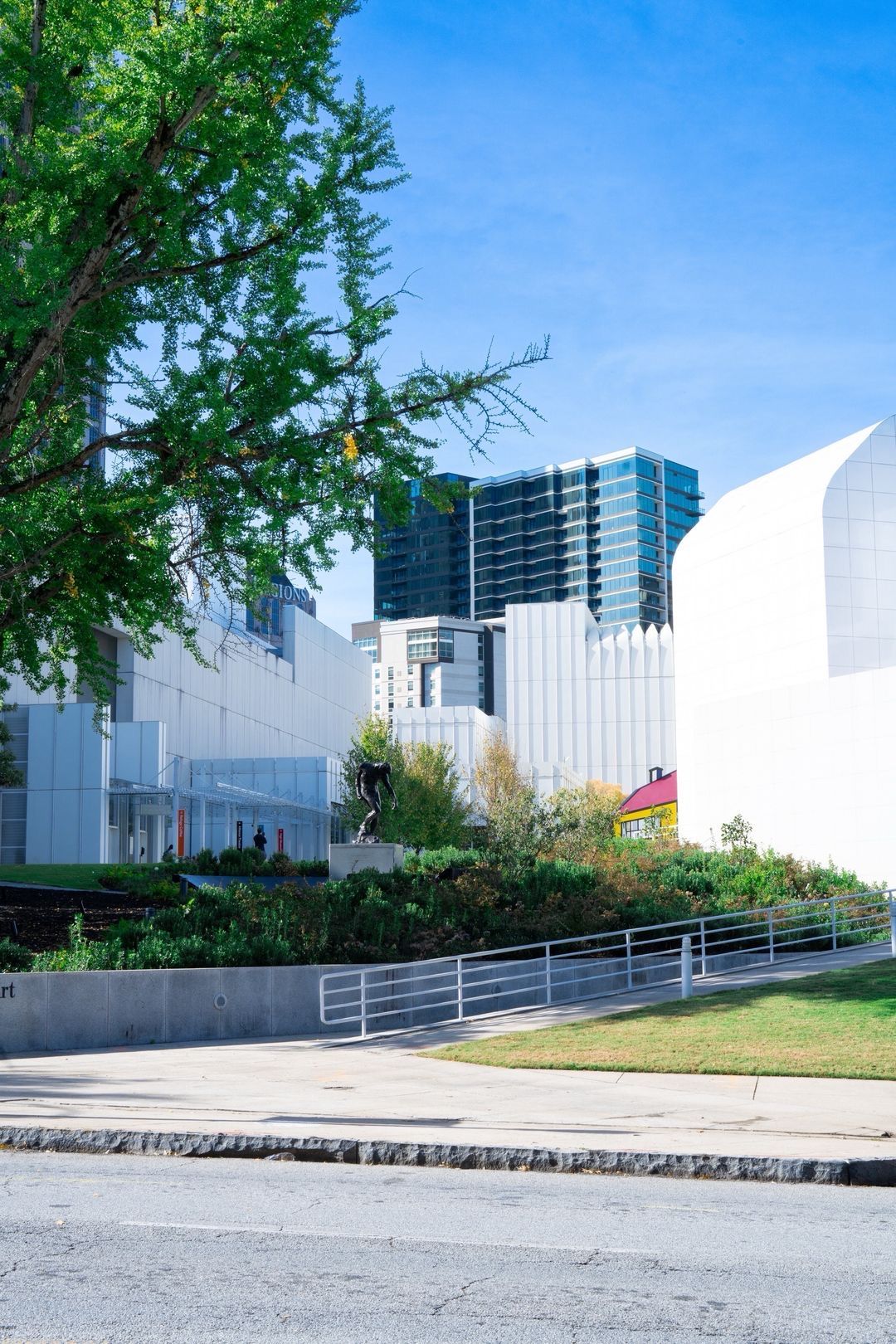 Modern white museum building with curved architecture surrounded by green trees and city skyscrapers under a clear blue sky.