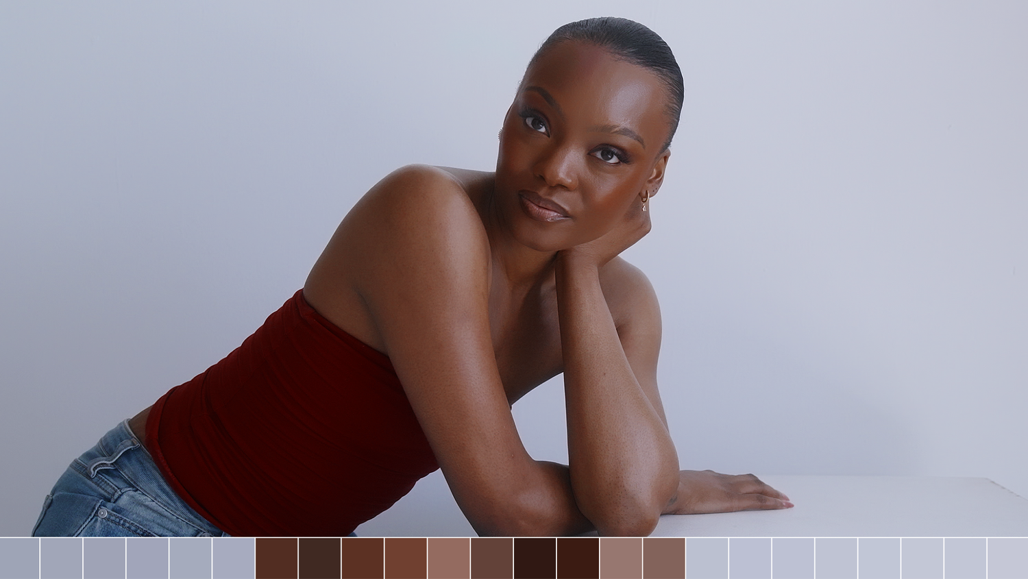 Elegant woman in red tube top leaning on white surface with warm skin tone color swatches below.
