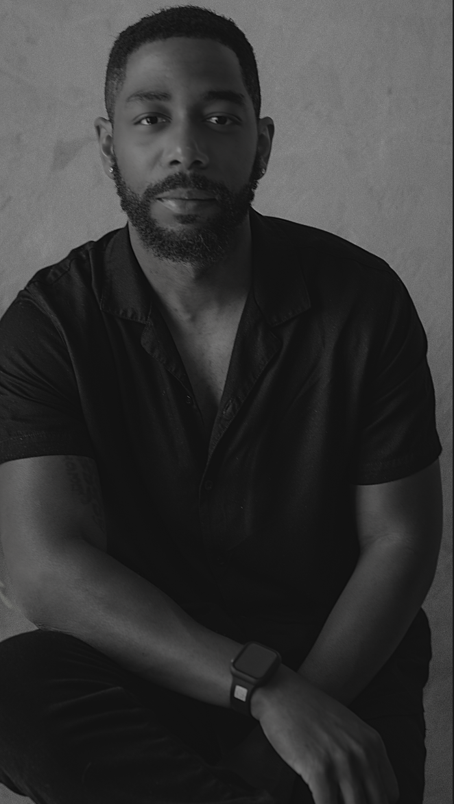 Black and white portrait of a bearded man in black shirt sitting in a relaxed pose.