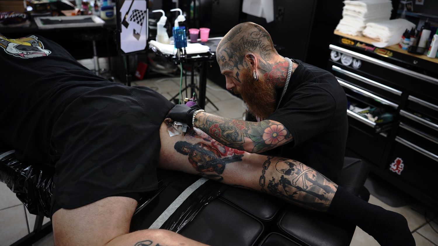 Tattoo artist in black shirt working on detailed tattoo design in a professional tattoo studio.