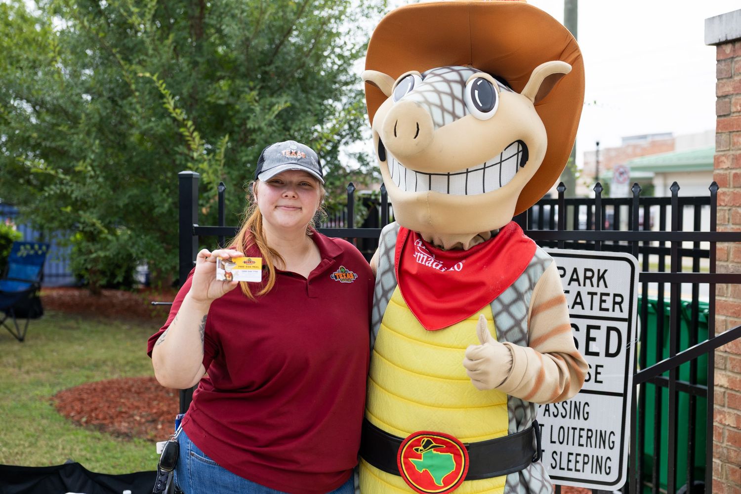 Woman in maroon shirt posing with colorful armadillo mascot statue at an outdoor event.