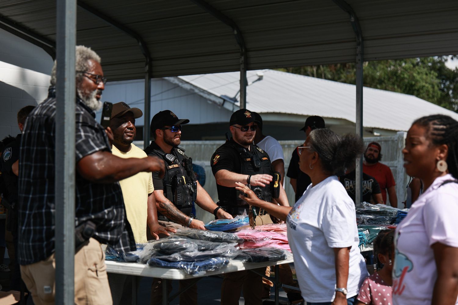Group of people in uniforms distribute clothing items at an outdoor community event tent.
