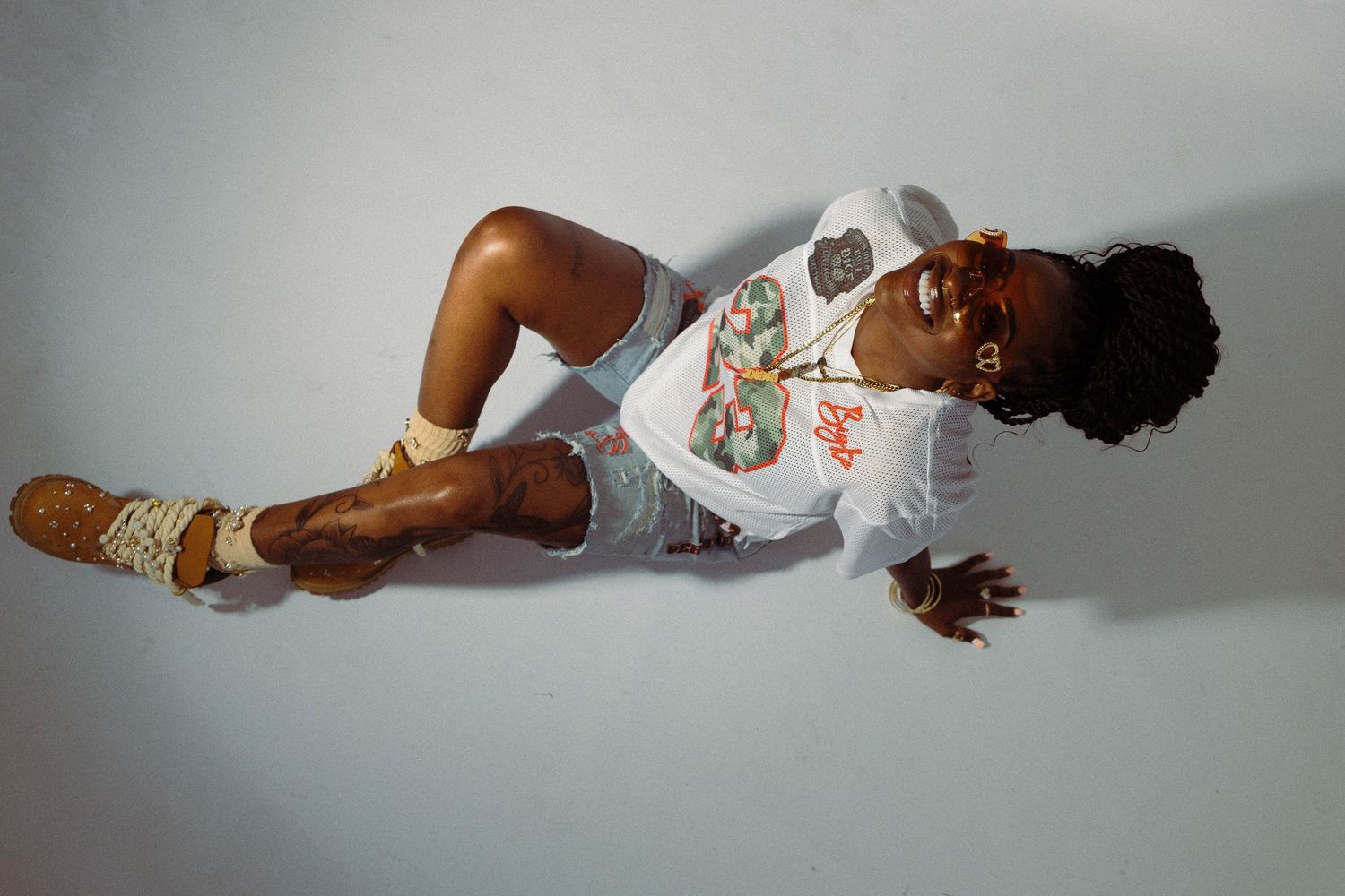 Young woman poses lying on floor wearing white graphic tee and denim shorts with brown boots.