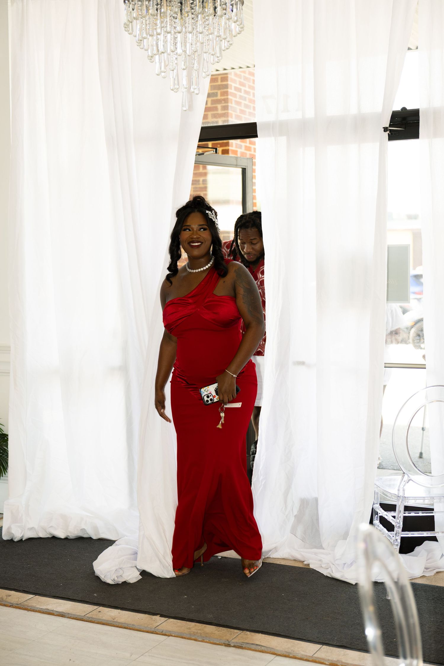 Woman in elegant red gown walking through white curtain doorway at a formal event.