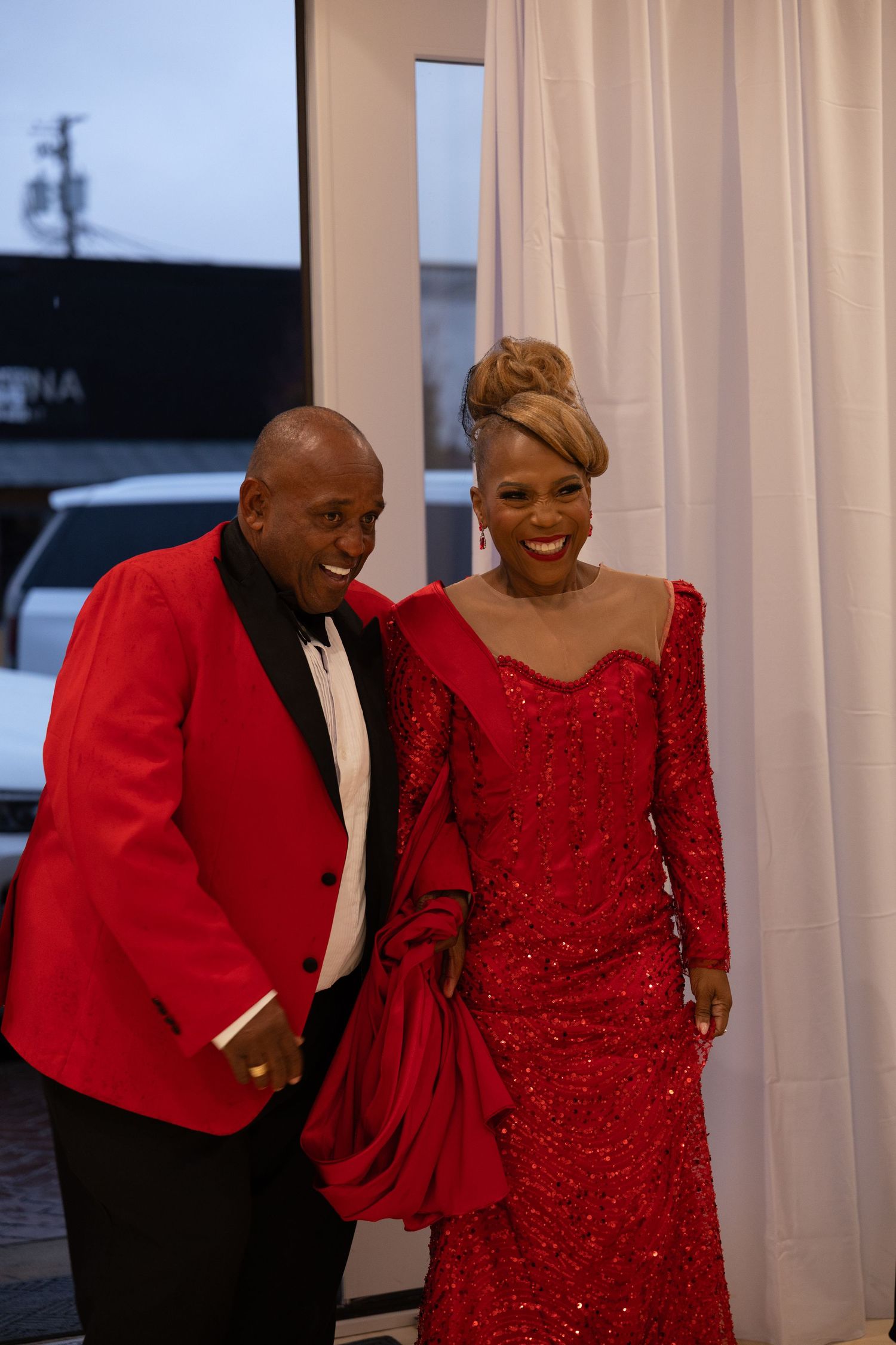 Couple dressed in matching red formal attire smiling together at an elegant evening event.