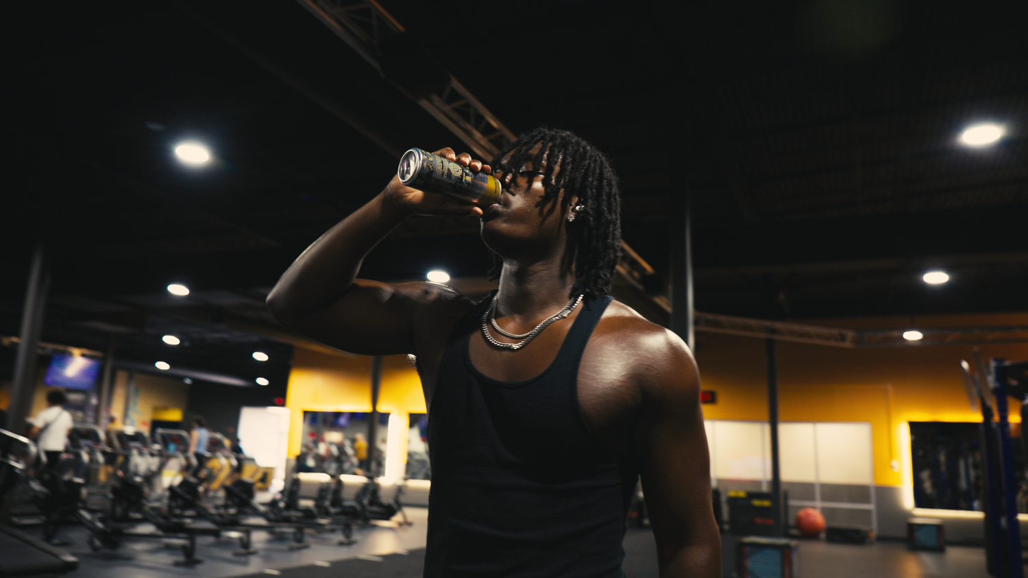 Athletic man drinking from bottle in modern gym with yellow and black decor after workout.