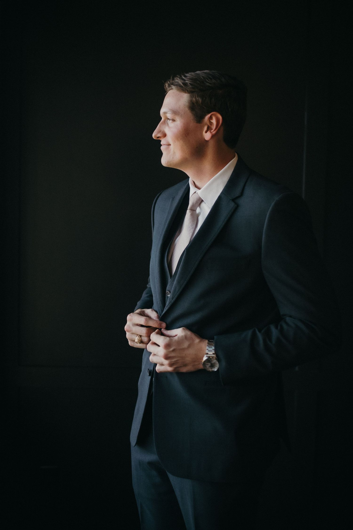 A groom adjusts his tie and jacket in a series of dark moody portraits.