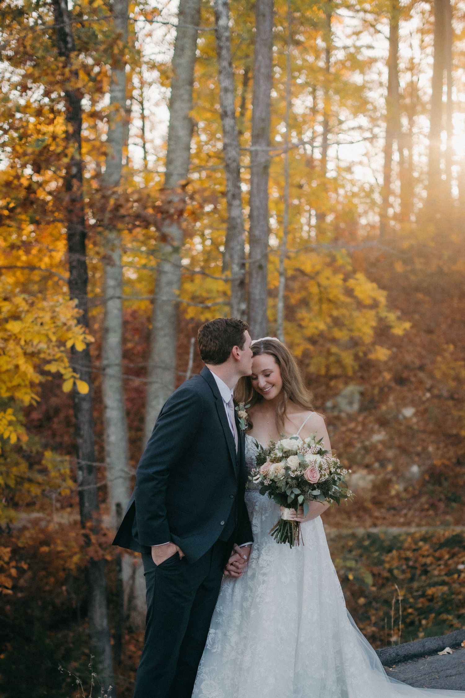 Newlyweds share an intimate moment in a sunlit autumn forest with birch trees.